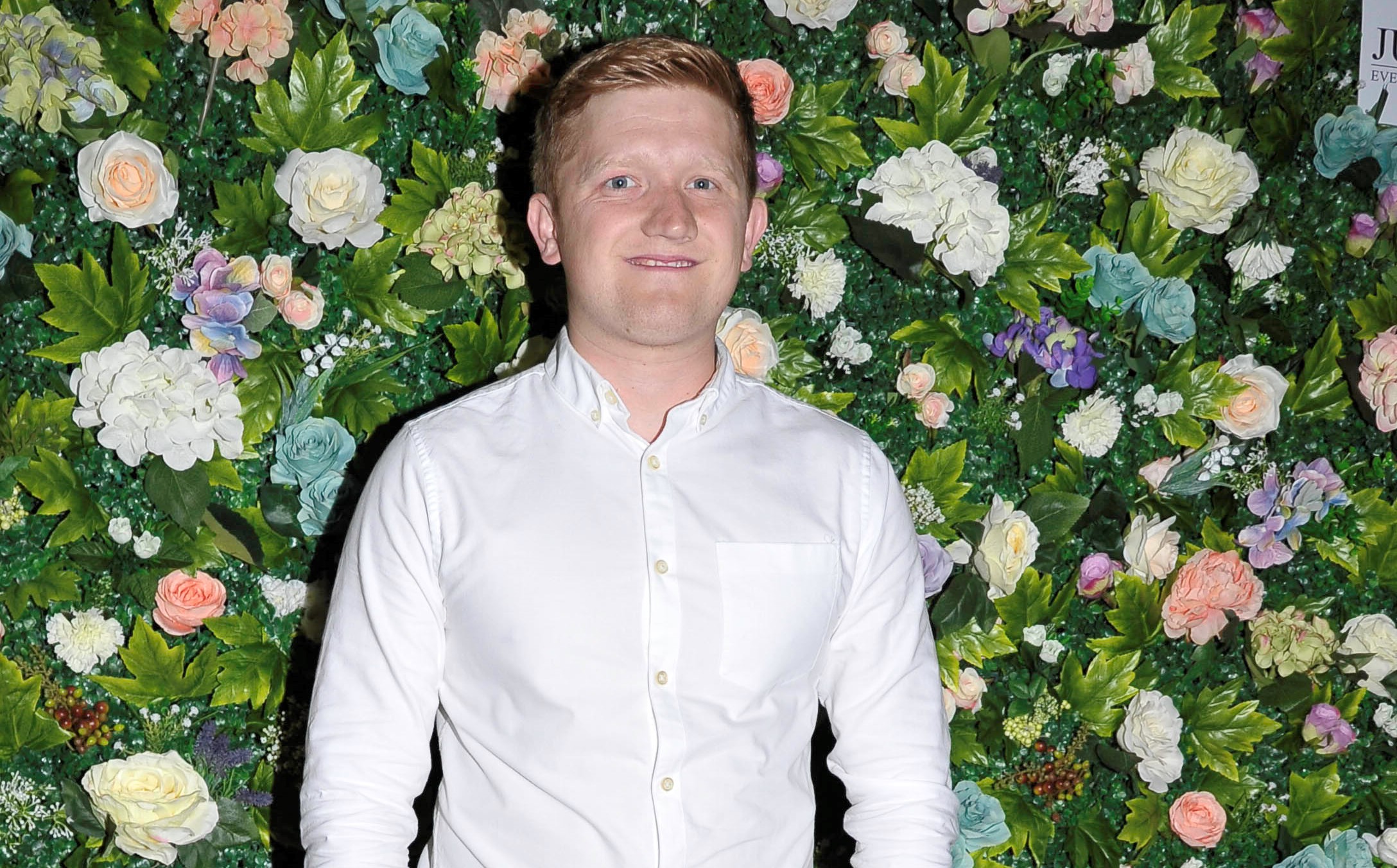 Coronation Street star Sam Aston Aka Chesney Brown poses in front of a wall of flowers at Katie McGlynn's leaving do