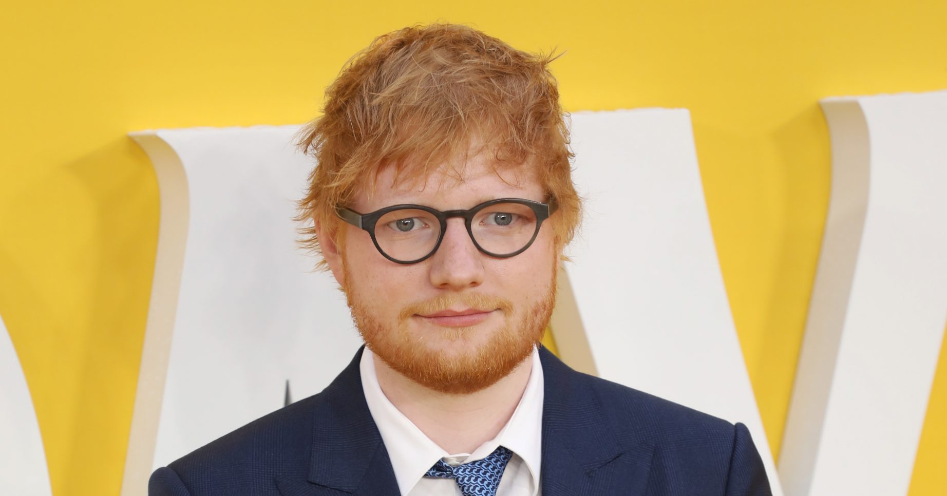 Ed Sheeran posing in a suit on a red carpet