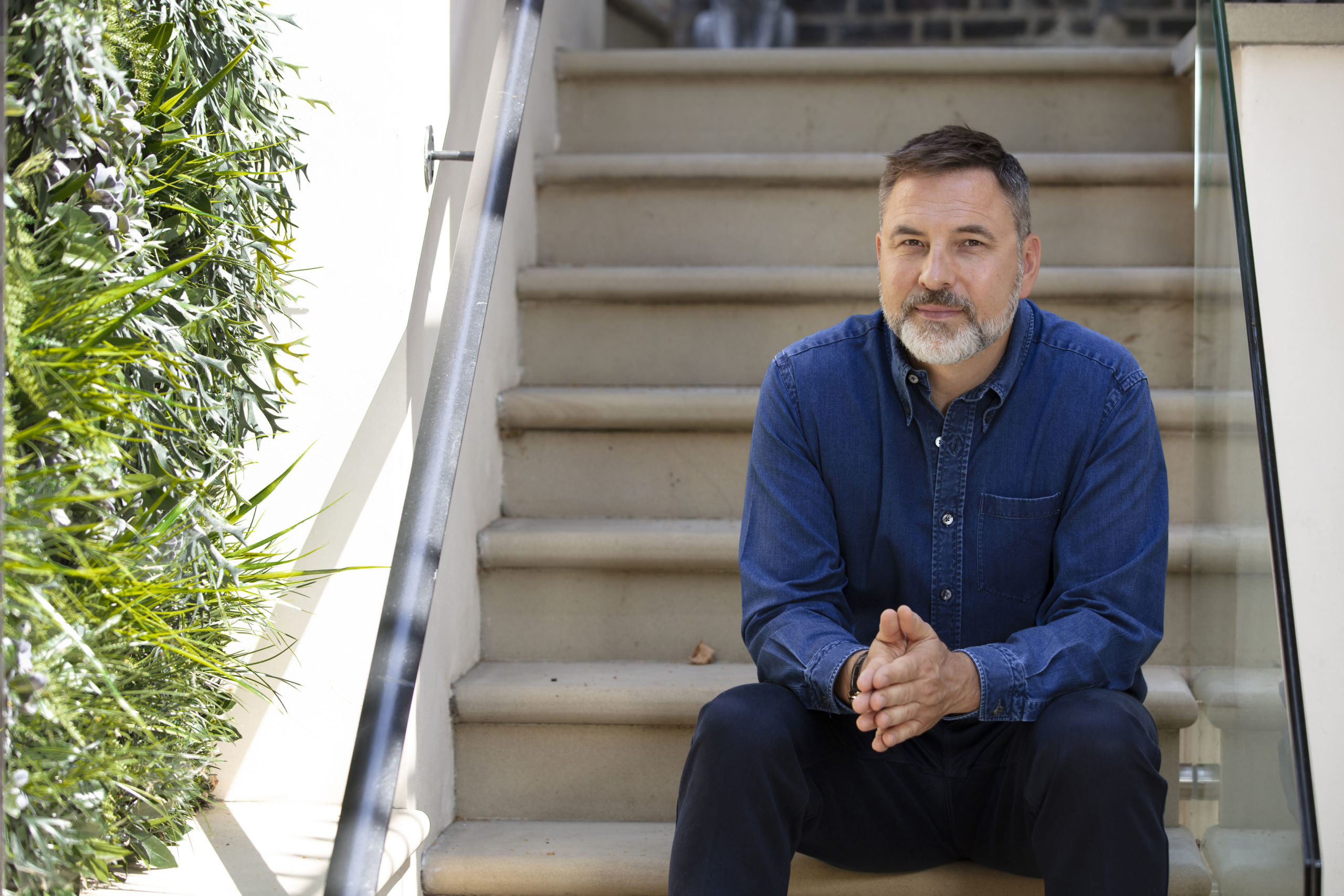 David Walliams sits on steps outside leafy house