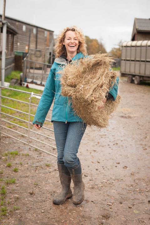 Kate Humble laughing holding a hay bale