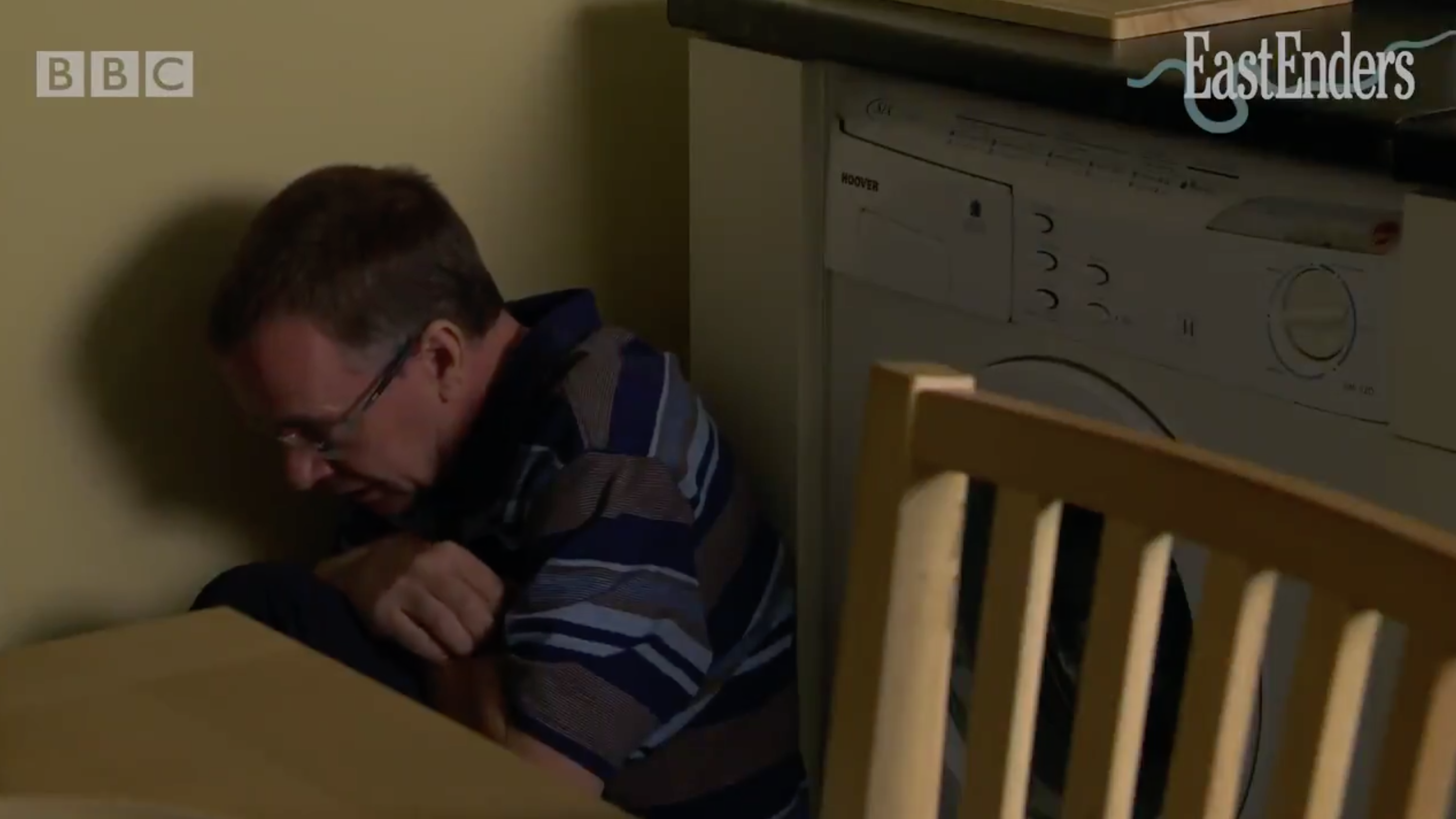 Ian Beale in EastEnders, cowering behind a table