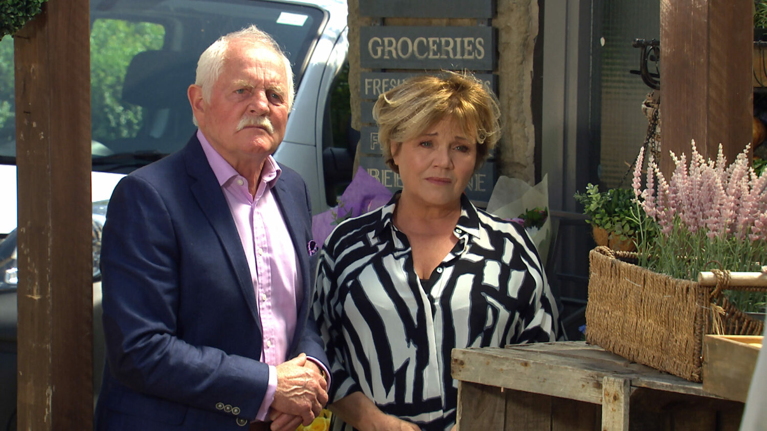 Eric Pollard looks cross as Brenda Walker looks sympathetic outside the shop in Emmerdale