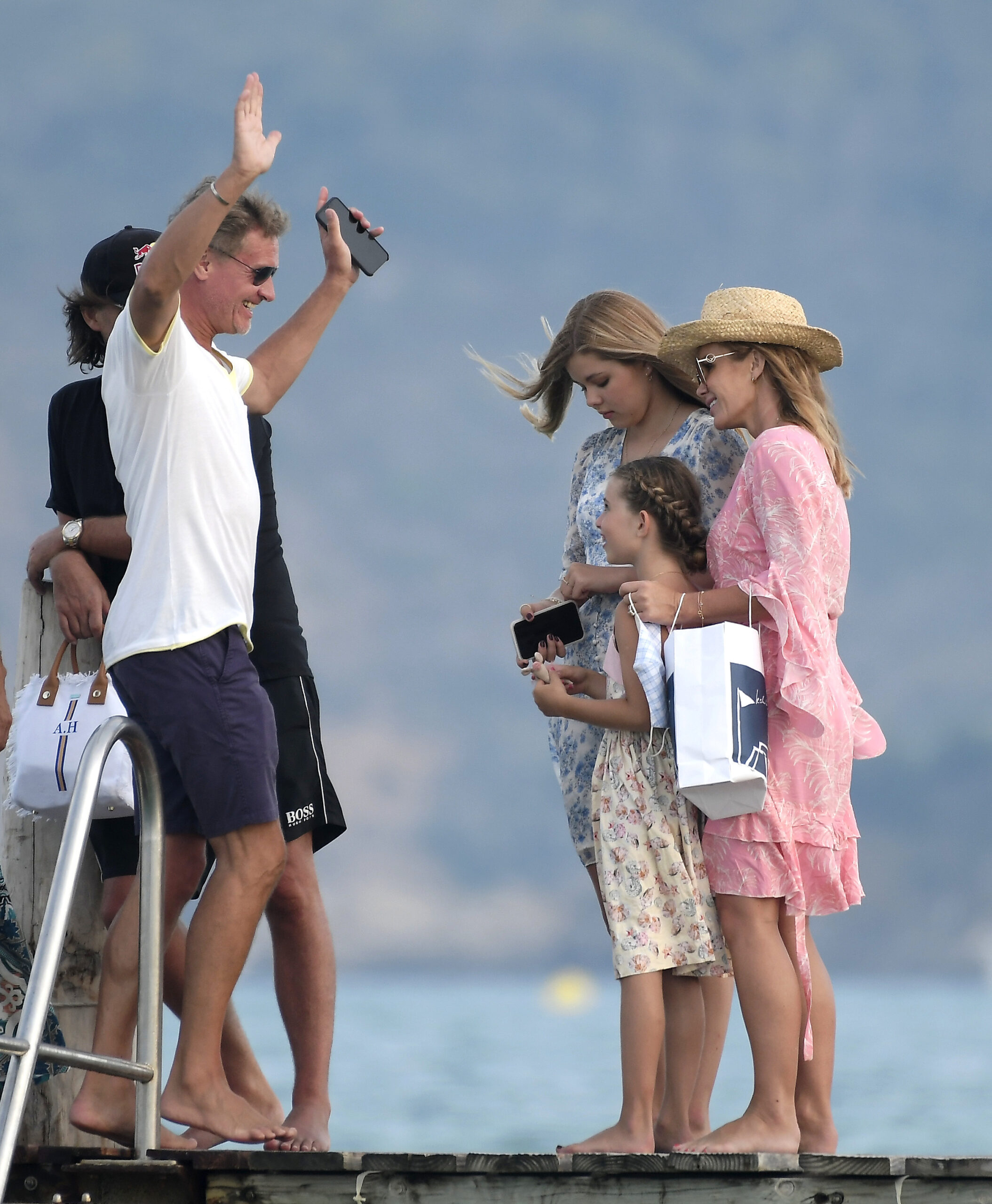 Amanda Holden in a pink kaftan and straw hat on a beach jetty with her husband chris hughes and daughters Alexa and Hollie