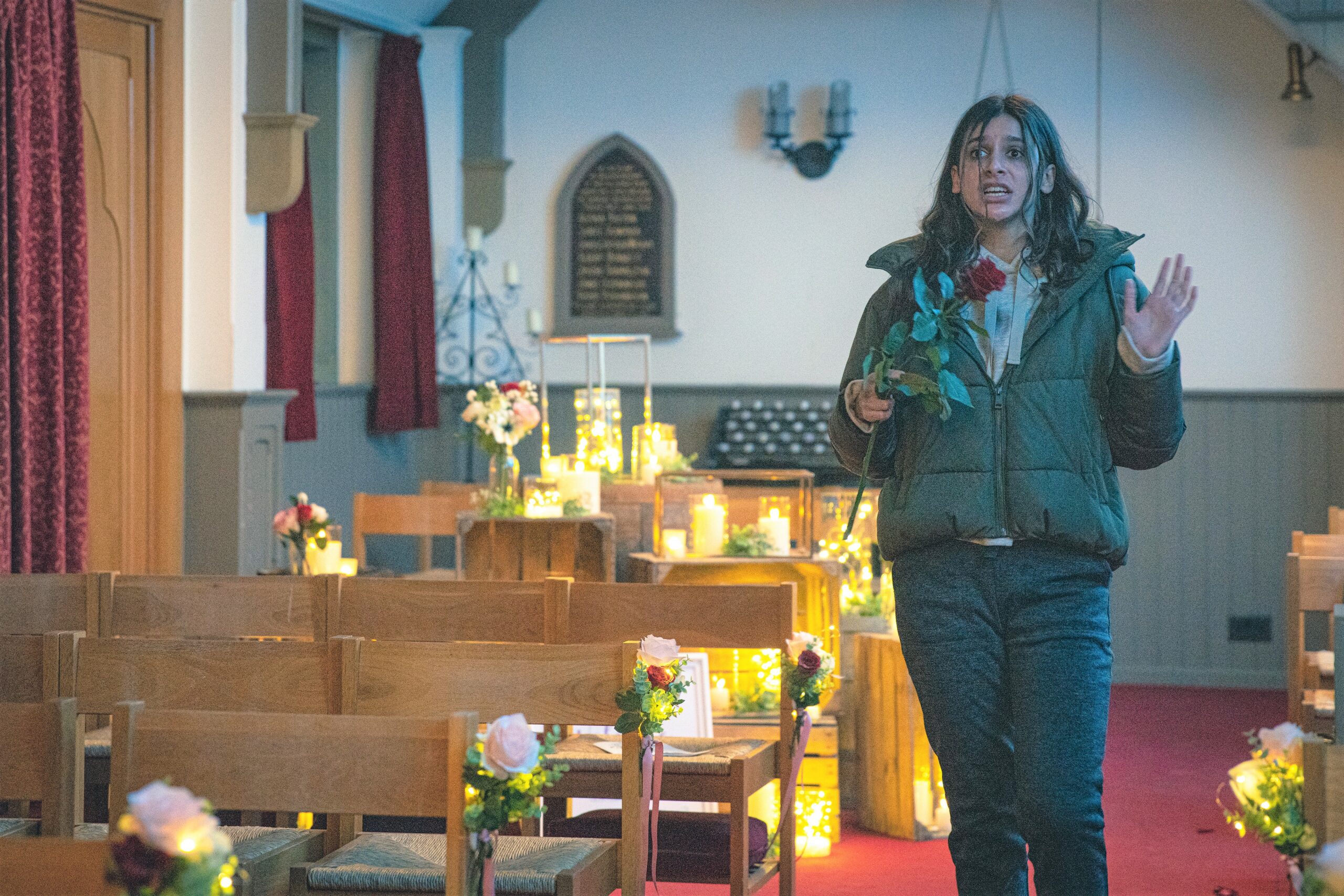 Emmerdale Meena in the candlelit church with a rose clearly talking to herself madly