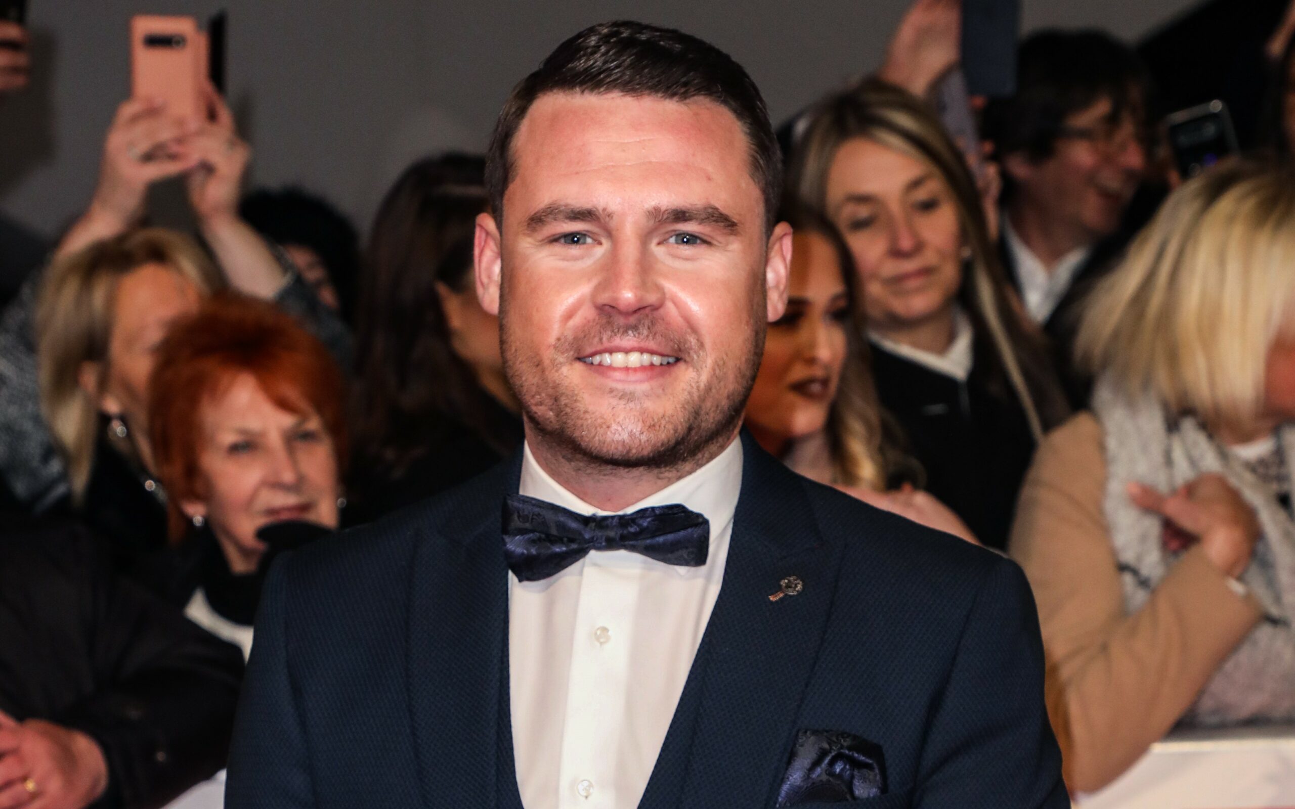 Danny Miller smiles in a suit and bow tie on the NTA red carpet