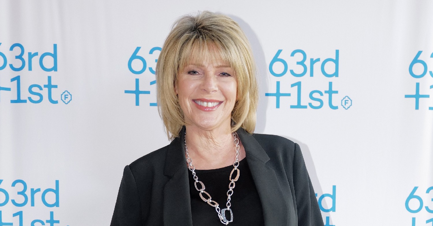 Ruth Langsford, wearing a black suit jacket and black top, smiling at the camera, with a white background