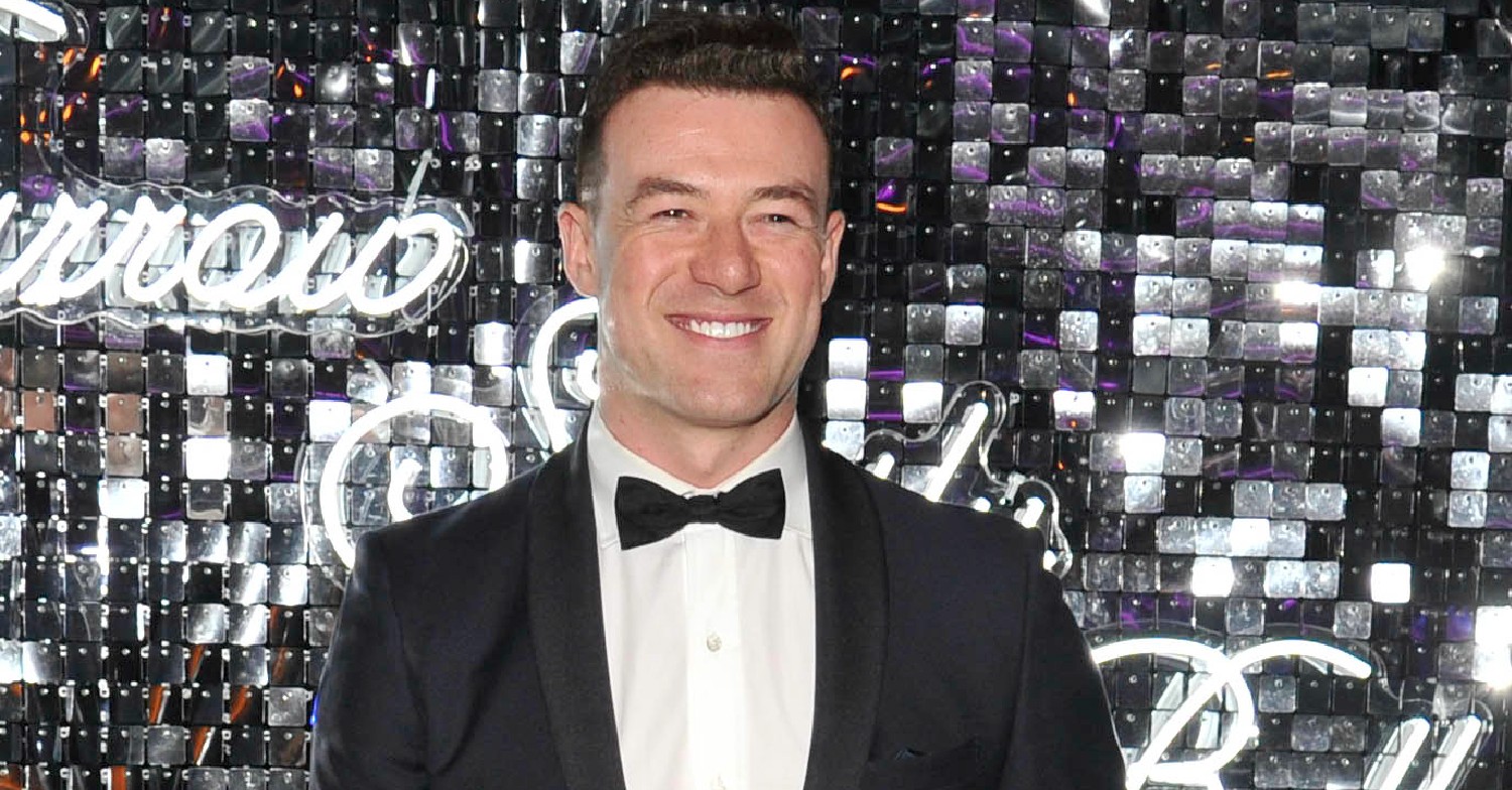 Kai Widdrington in a tuxedo smiling for the cameras in front of a sparkly background
