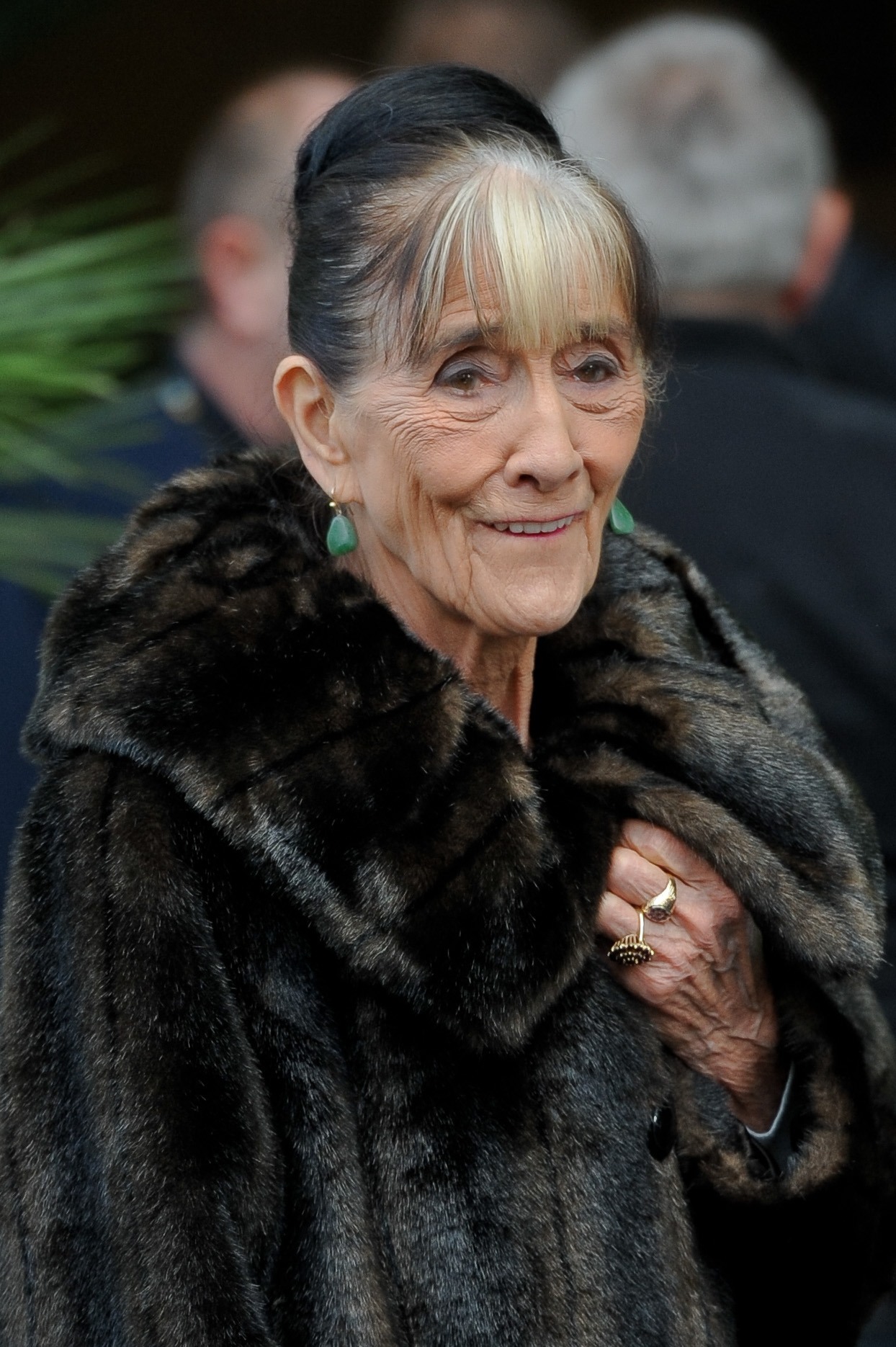 June Brown wearing a fur coat with blonde hair