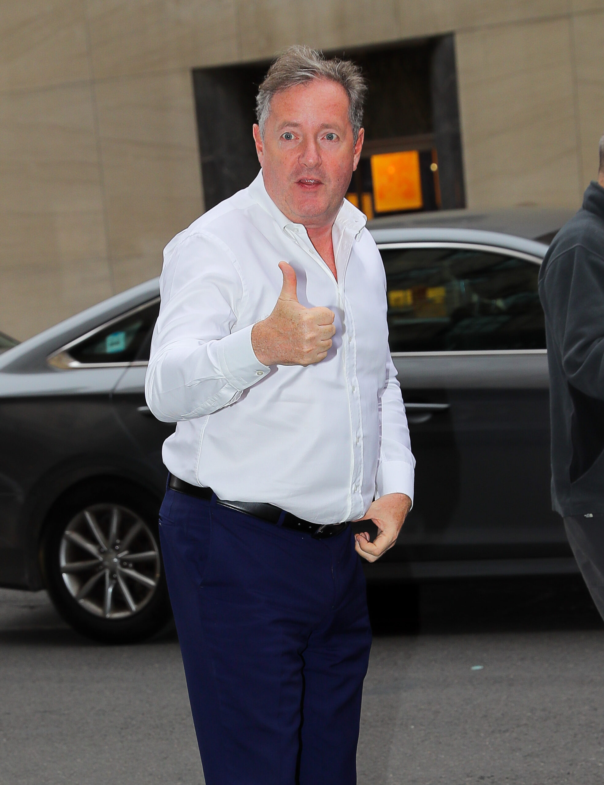 Piers Morgan puts thumb up to cameras in white shirt