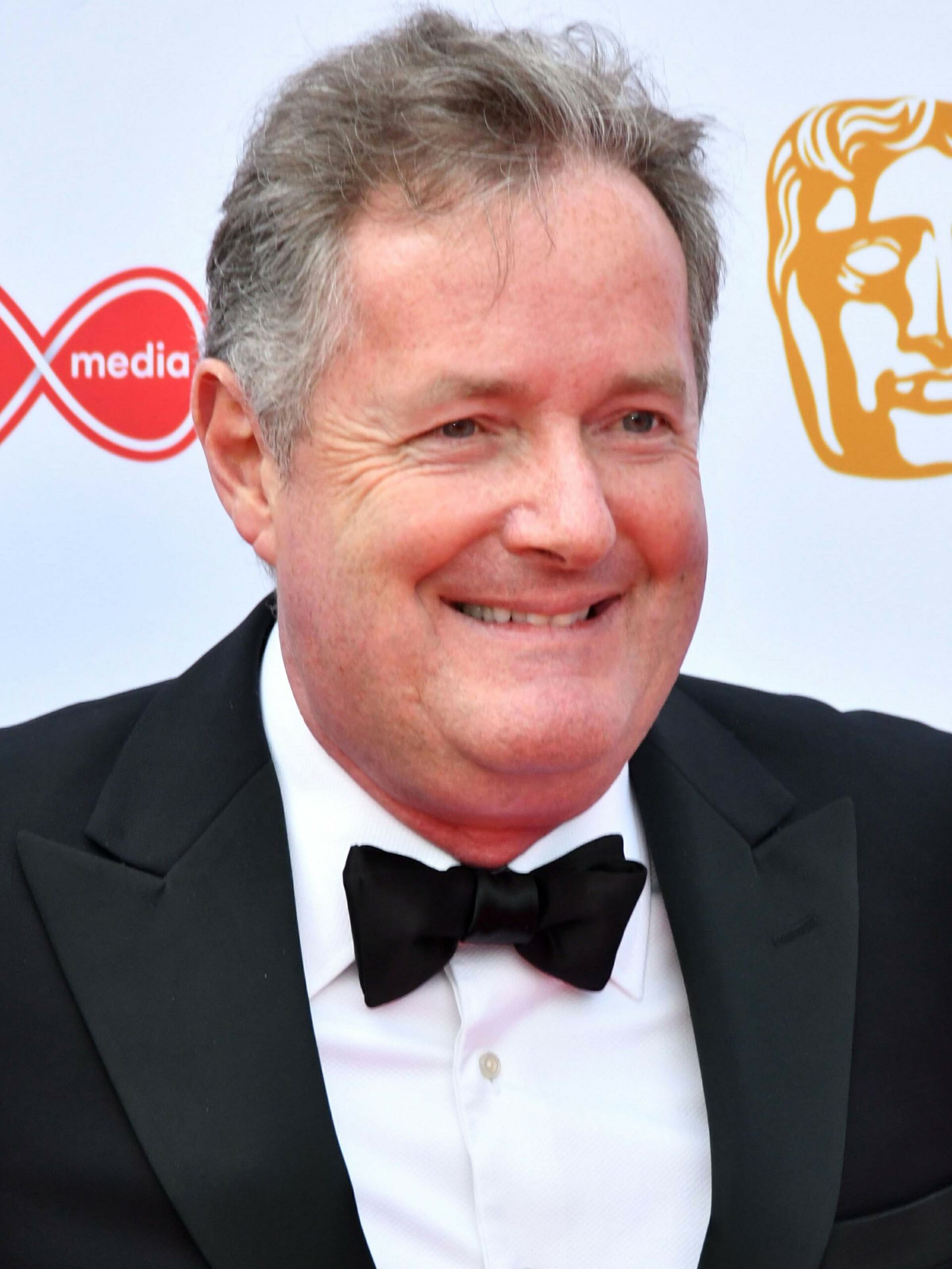 Piers Morgan smiles in black suit at BAFTAs