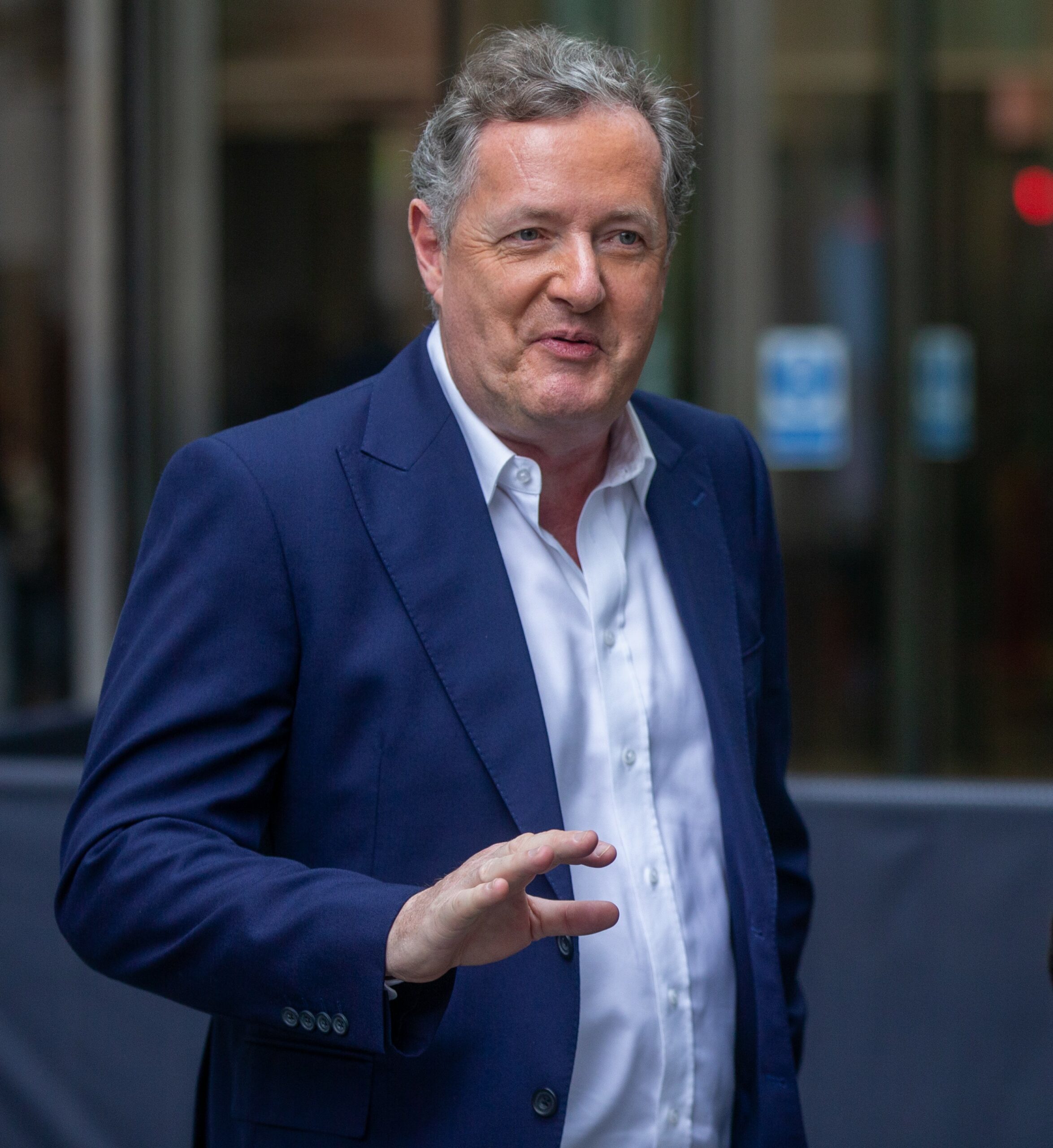 Piers Morgan smiles and waves in blue suit