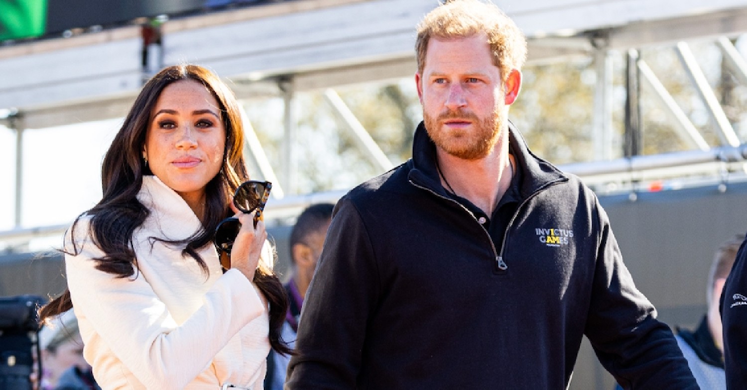 Prince Harry and Meghan Markle casual wear holding hands looking away from camera