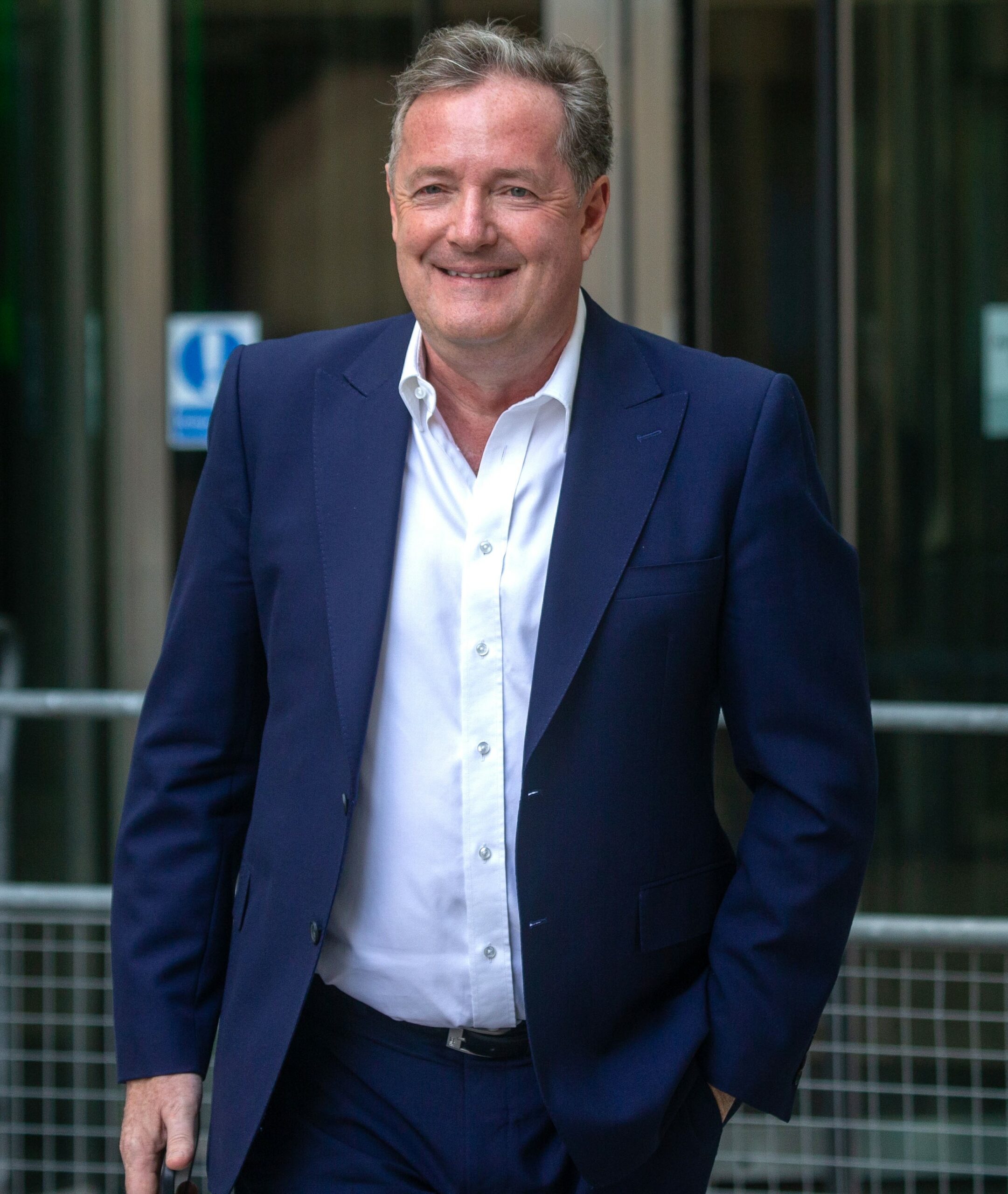 Piers Morgan in navy suit smiling outside TV studios
