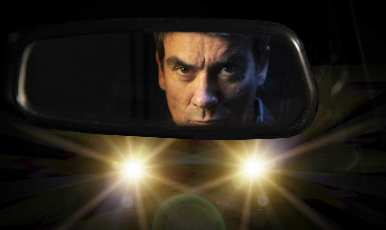 Cain Dingle shown looking murderous in a car rear view mirror with headlights blaring behind him