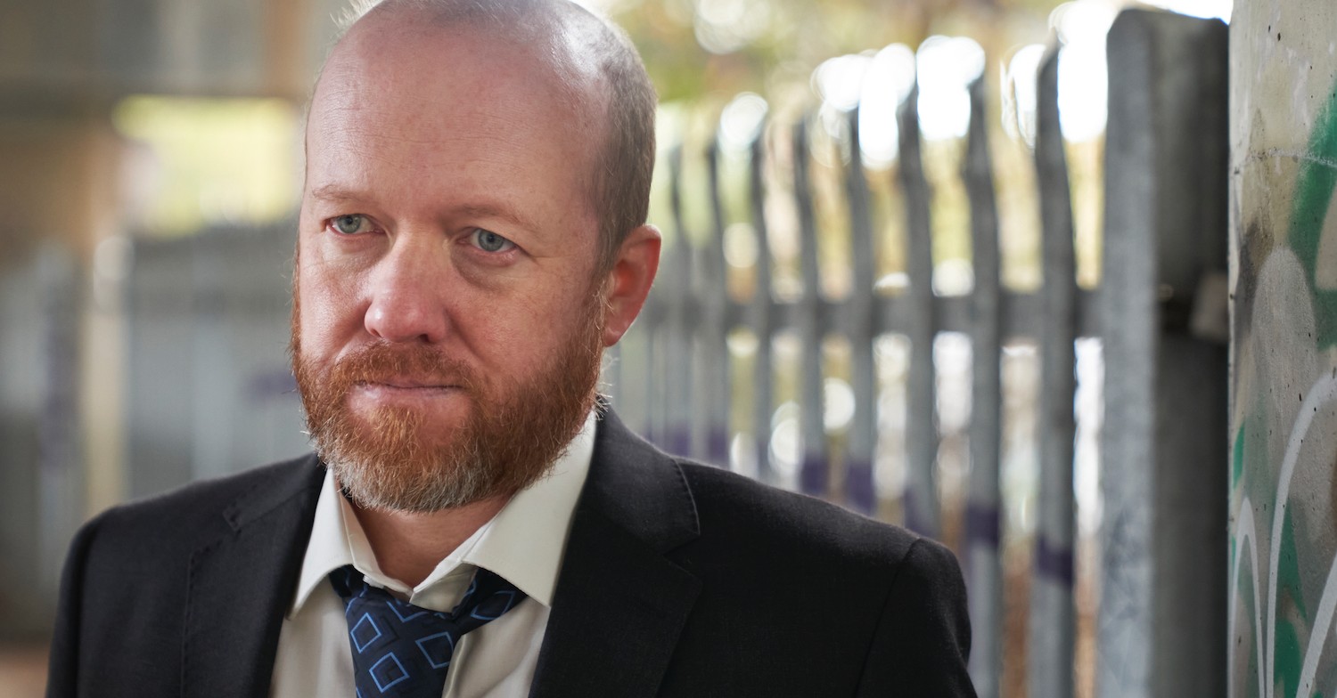 Steve Oram in DI Ray in suit and tie in front of some lockers