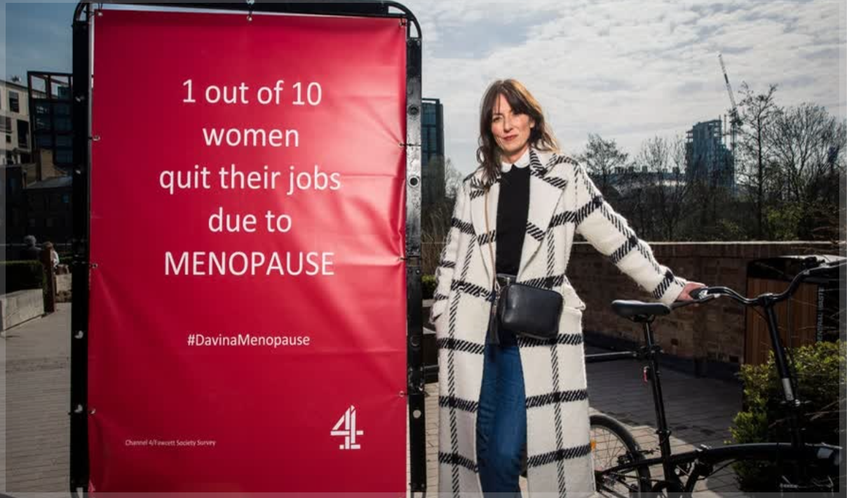 Davina McCall standing next to a red poster about the menopause 