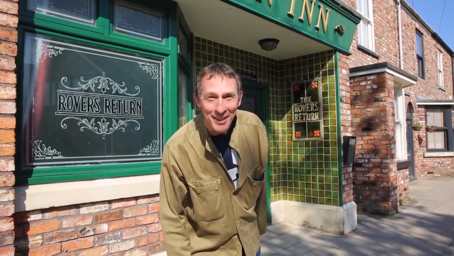 Coronation Street Spider smiles as he stands outside the Rover and announces his return