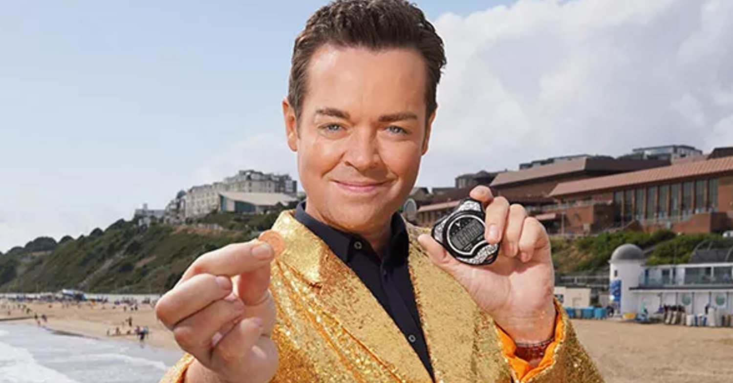 Stephen Mulhern smiling in a gold jacket on the beach