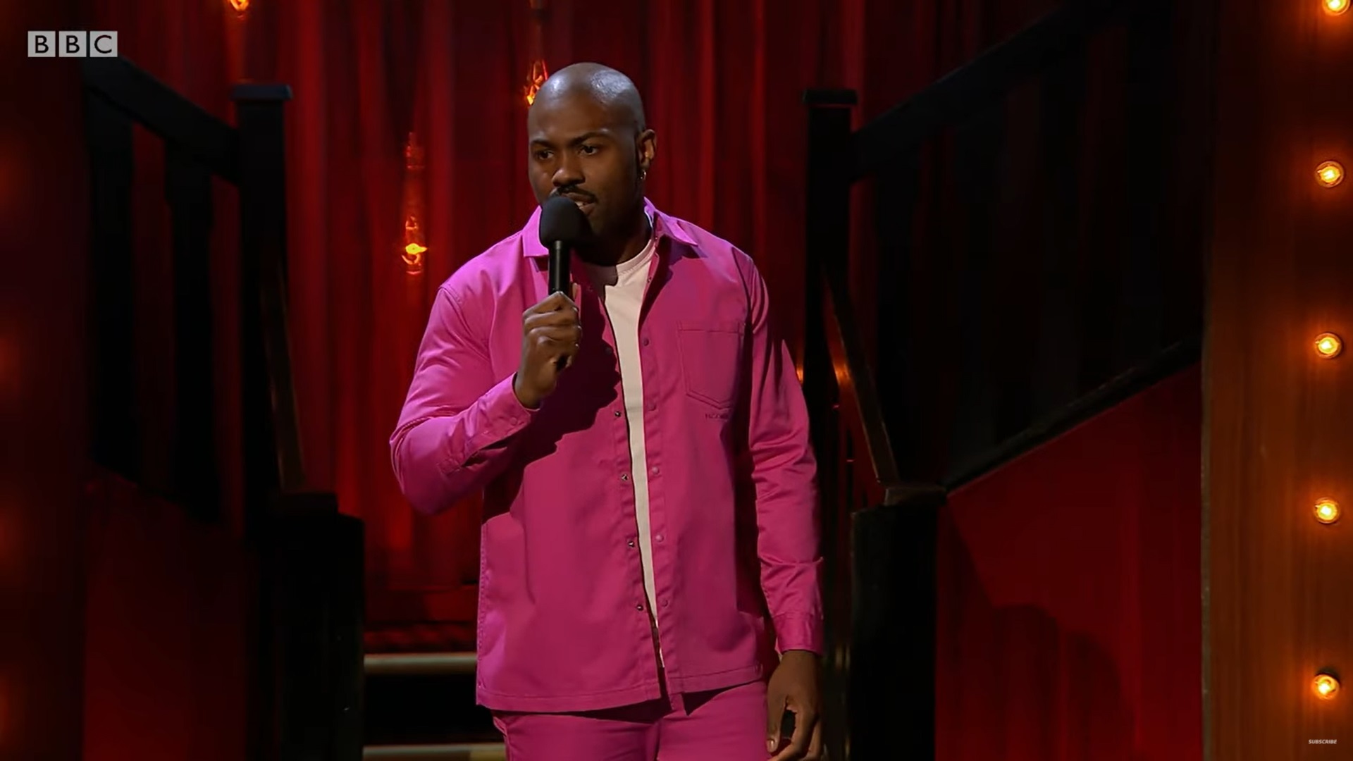 Darren Harriott on stage in a pink suit