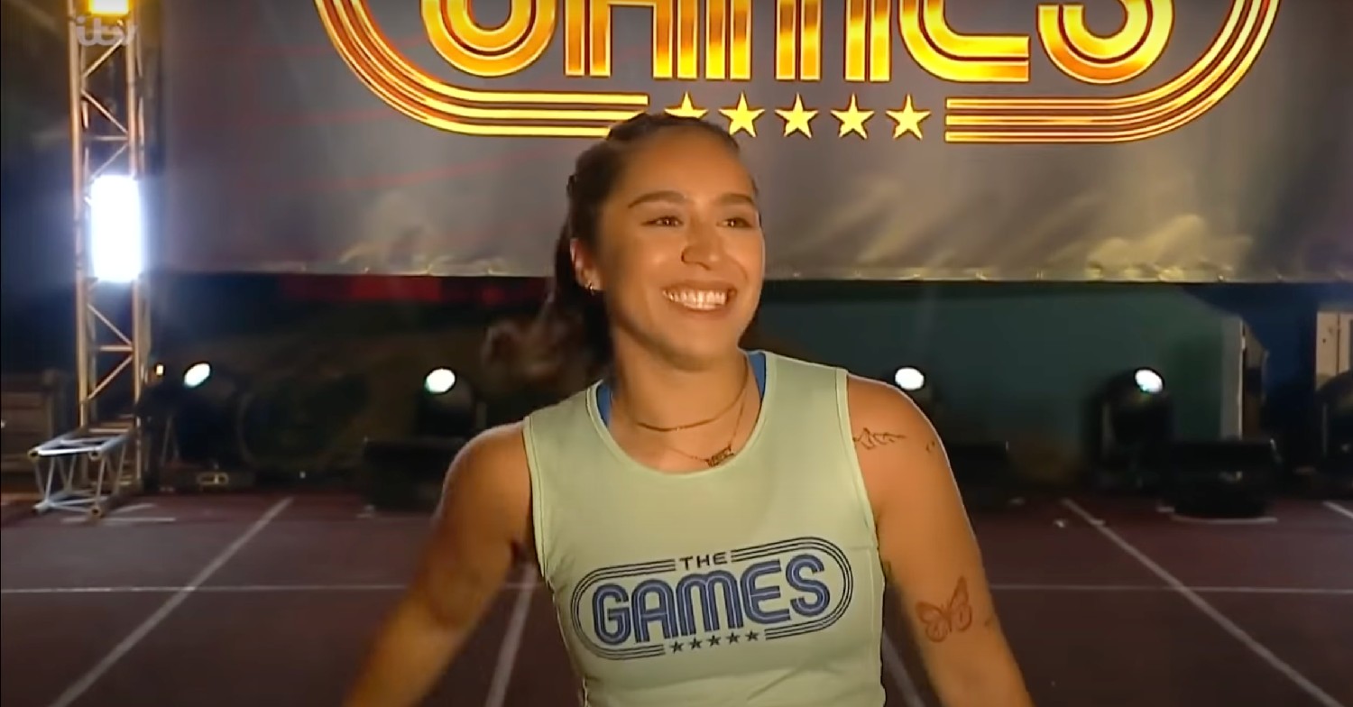 Chelcee Grimes wearing a pale blue vest, smiling on an athletics track on The Games tv show