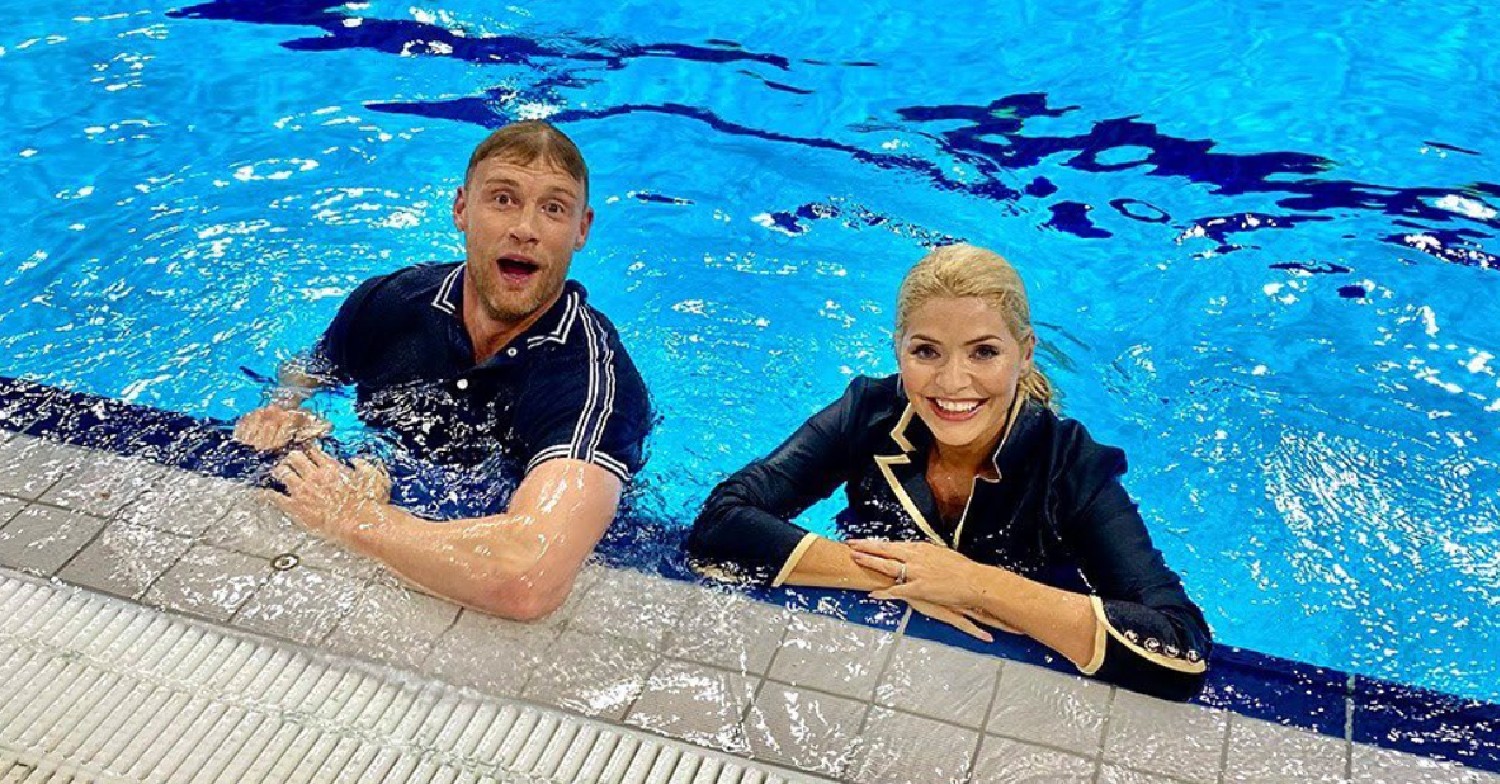 Holly Willoughby and Freddie Flintoff, in a swimmin gpool, fully clothed, smiling at the camera