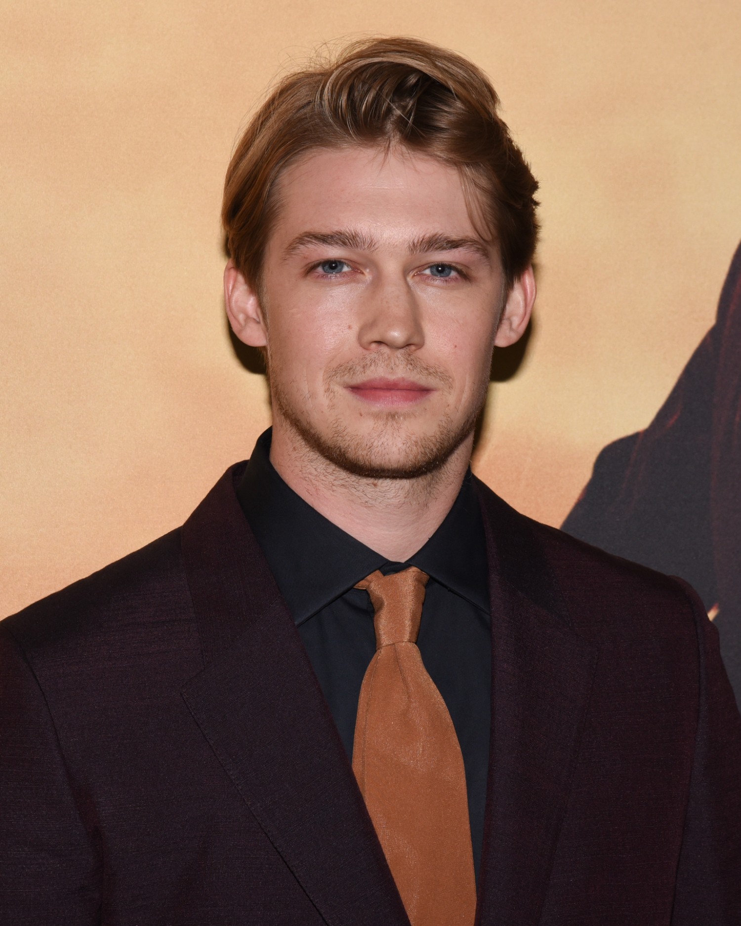 Joe Alwyn smiling weakly as he wears a dark suit