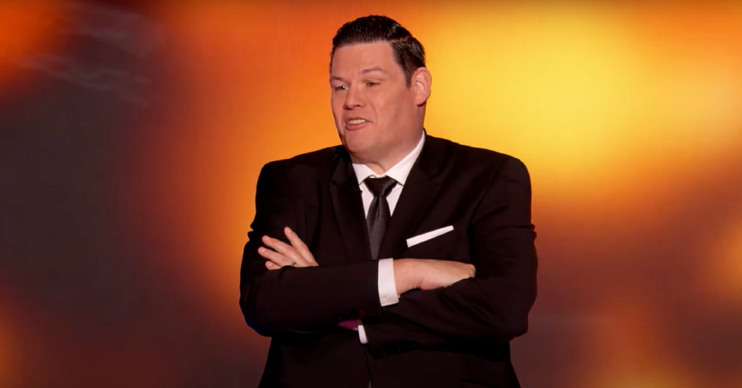 Mark Labbett with his arms folded on an orange background on the Chase USA