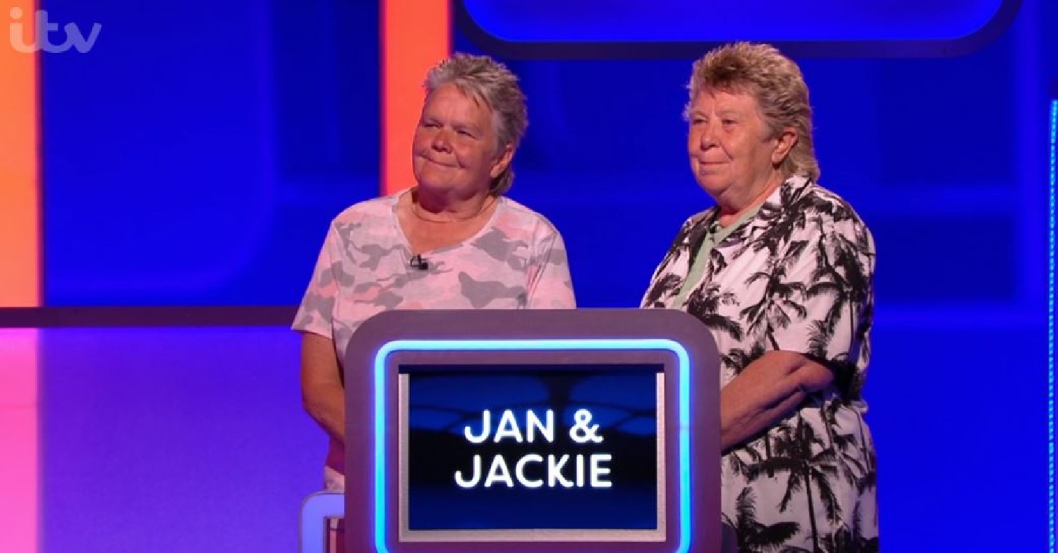 Jan and Jackie, standing behind a podium with their name on it on Lingo