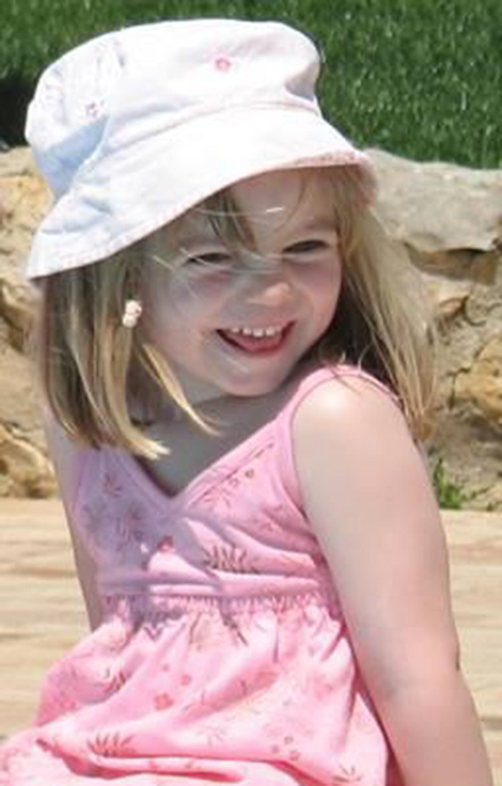 Madeleine McCann smiling in a pink hat
