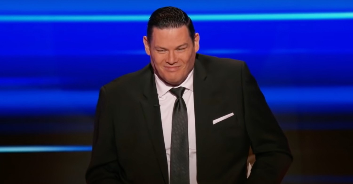 Mark Labbett in a suit and tie smirking on The Chase USA