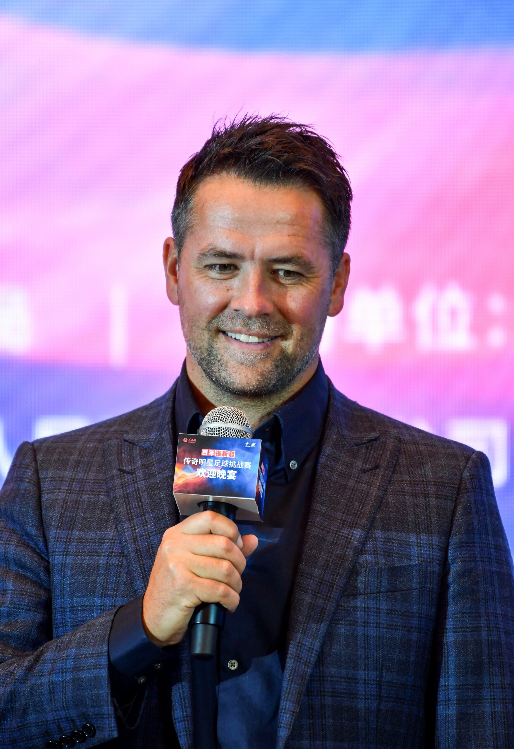 Michael Owen smiling and holding a microphone 