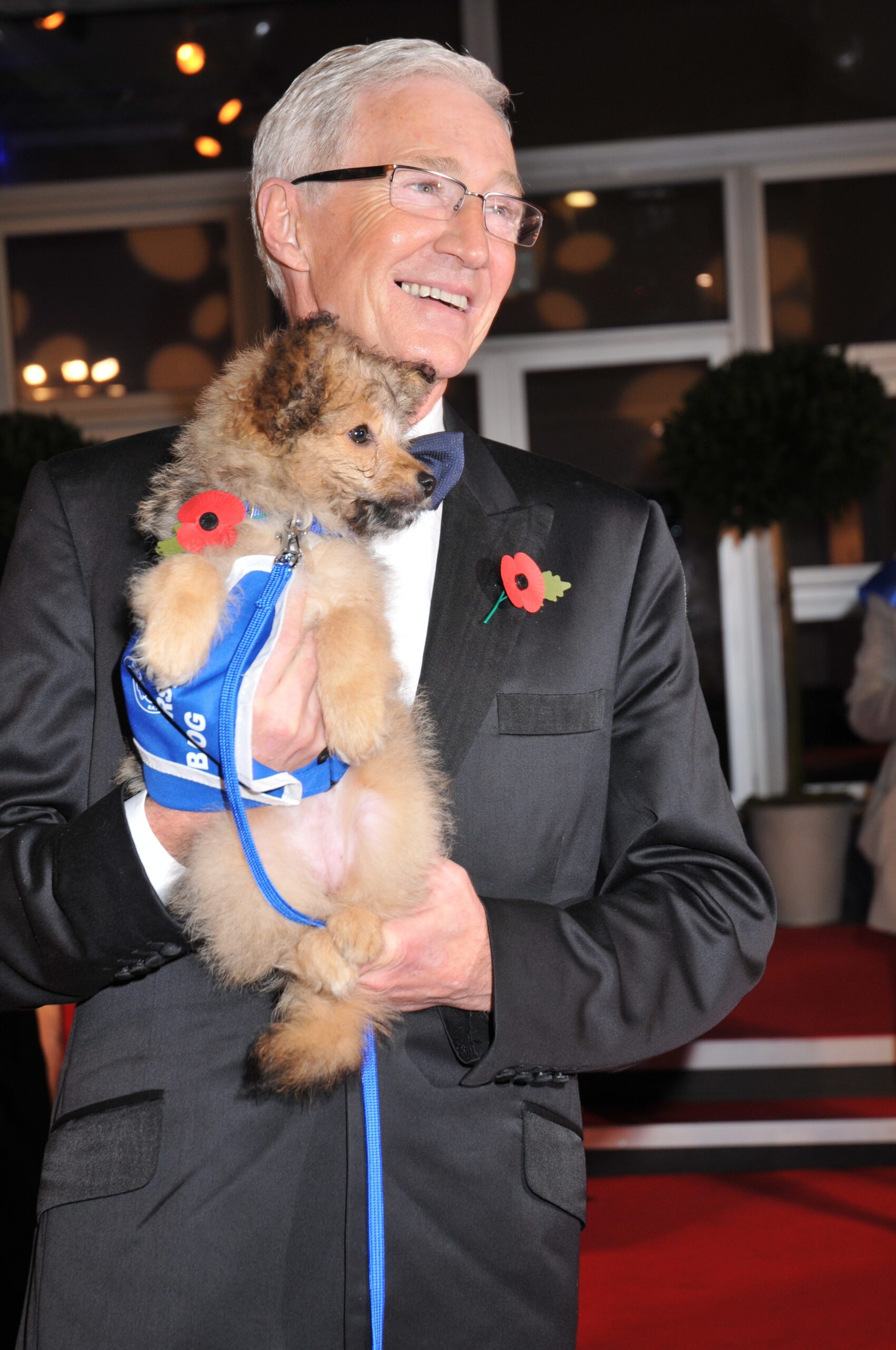 Paul O'Grady smiling and holding a dog on the red carpet