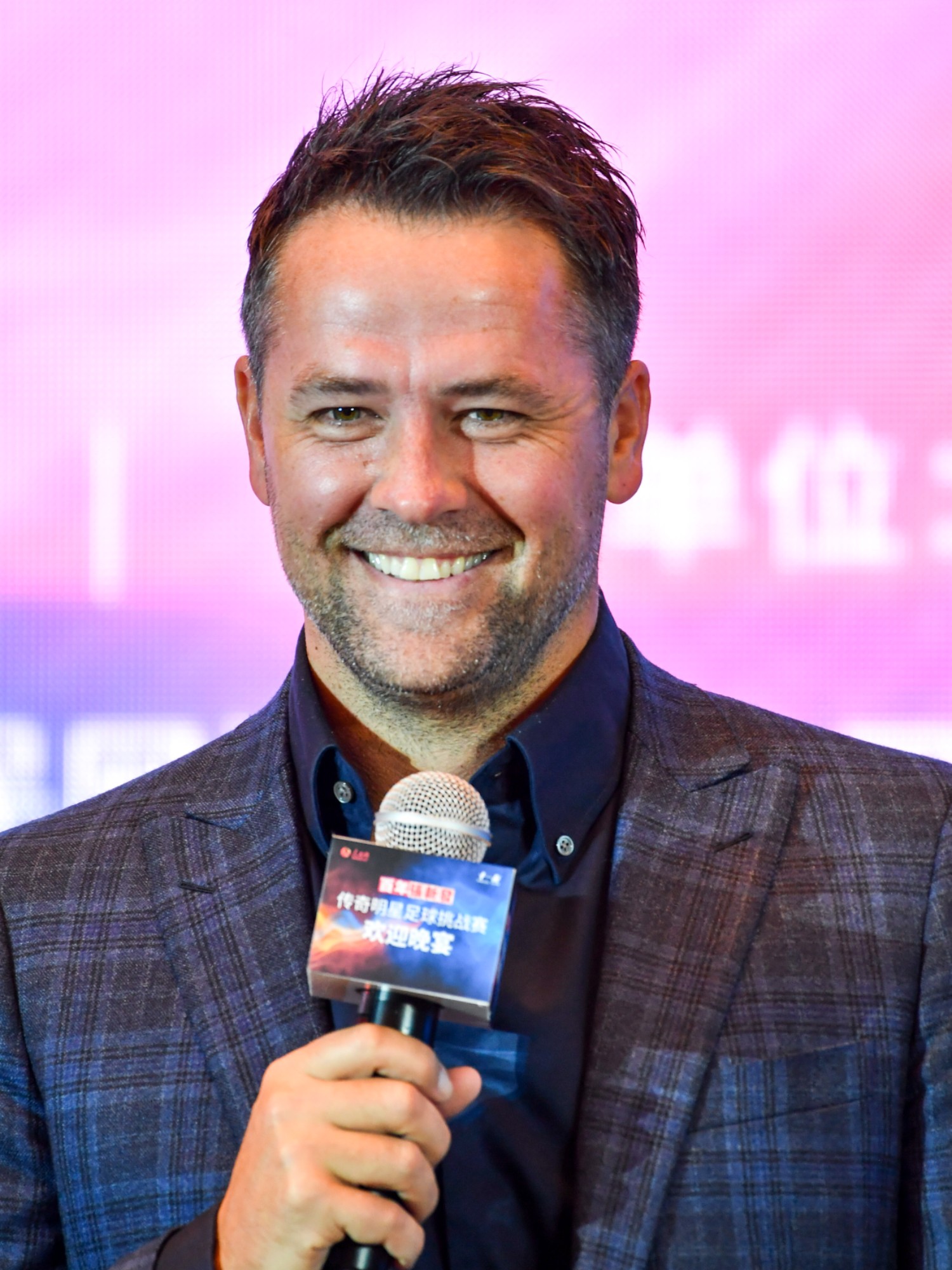 Michael Owen smiling and holding a microphone