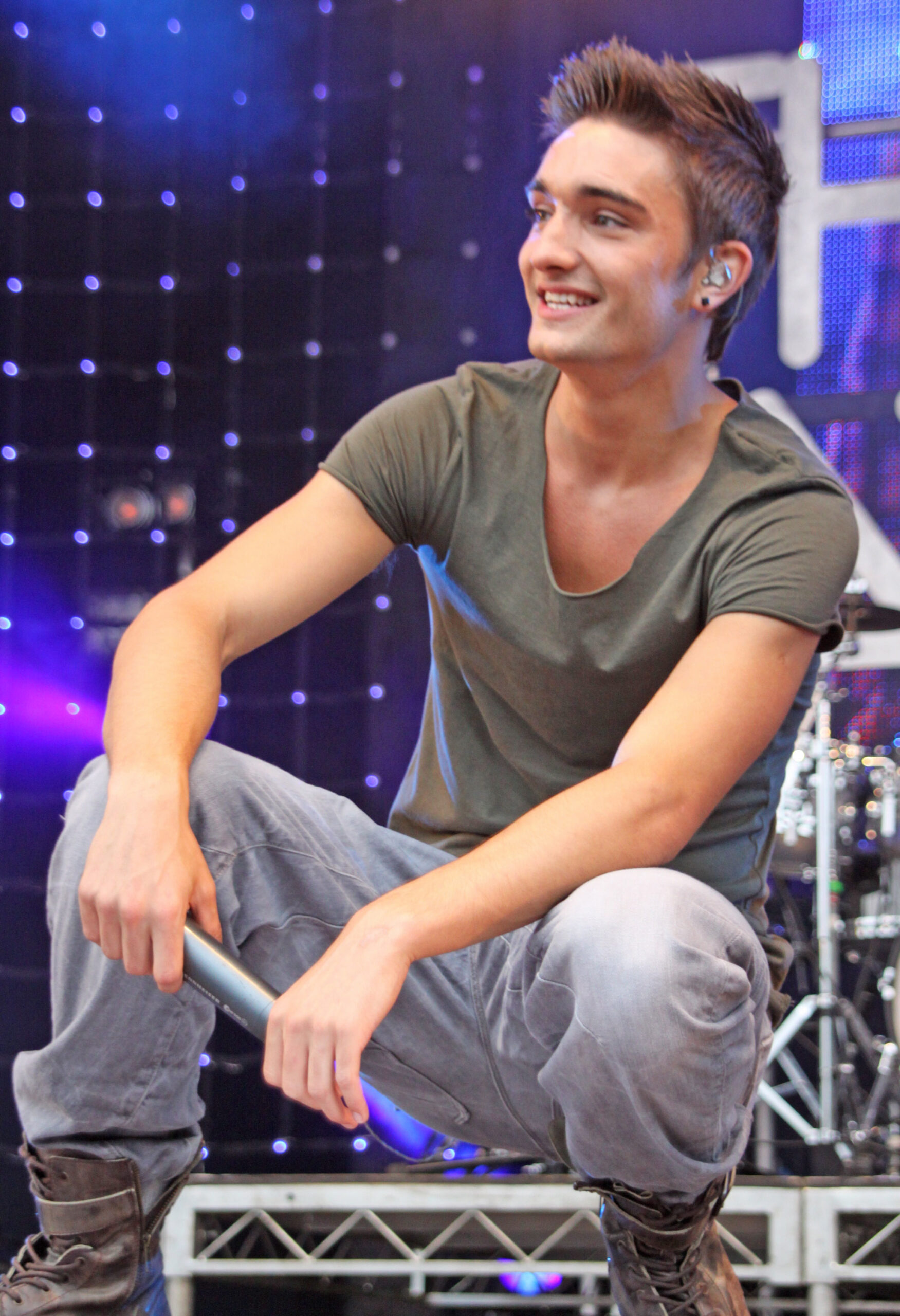 Tom Parker smiling as he crouches down on stage