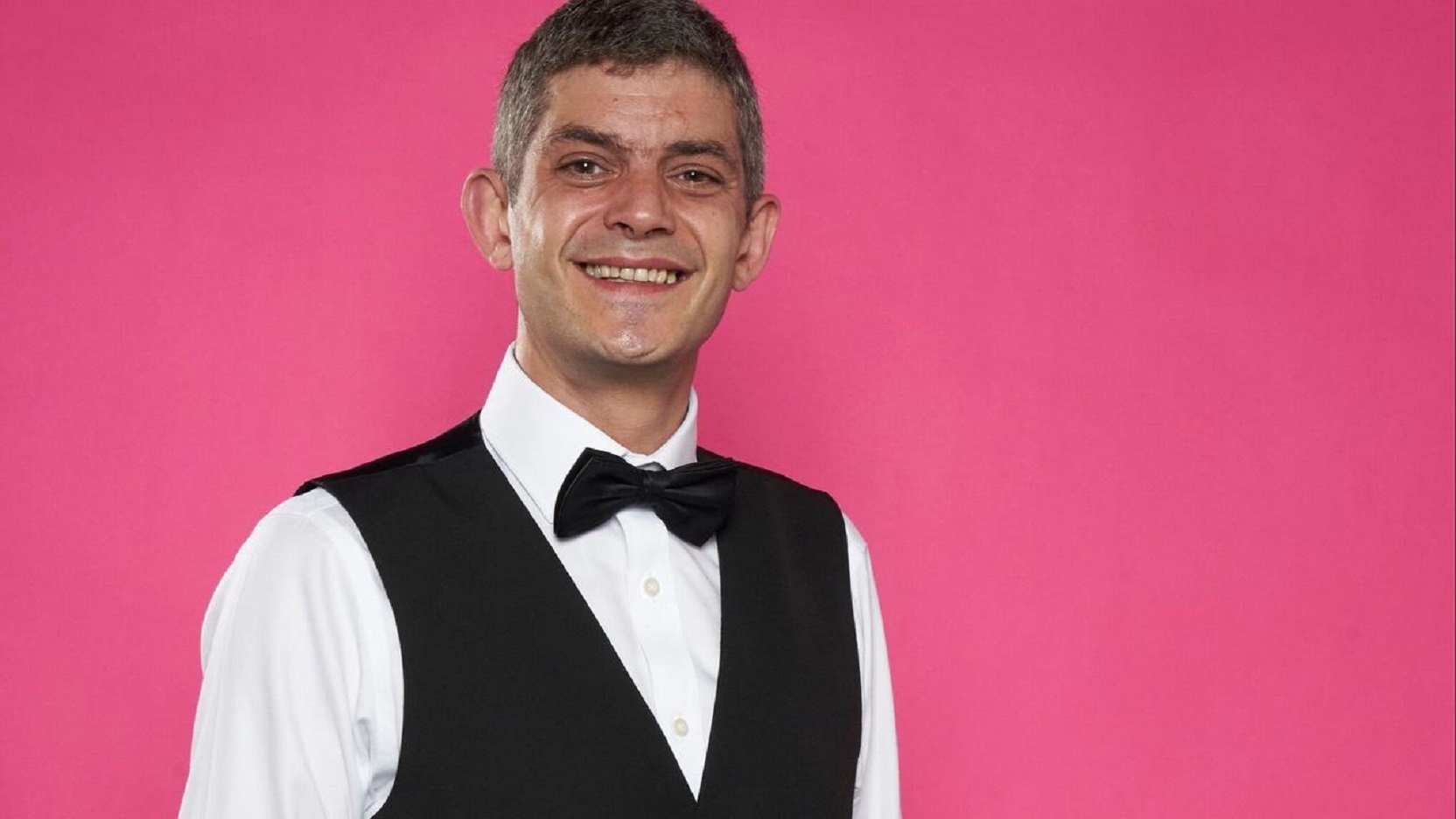 First Dates' Merlin in a bow tie against a pink background