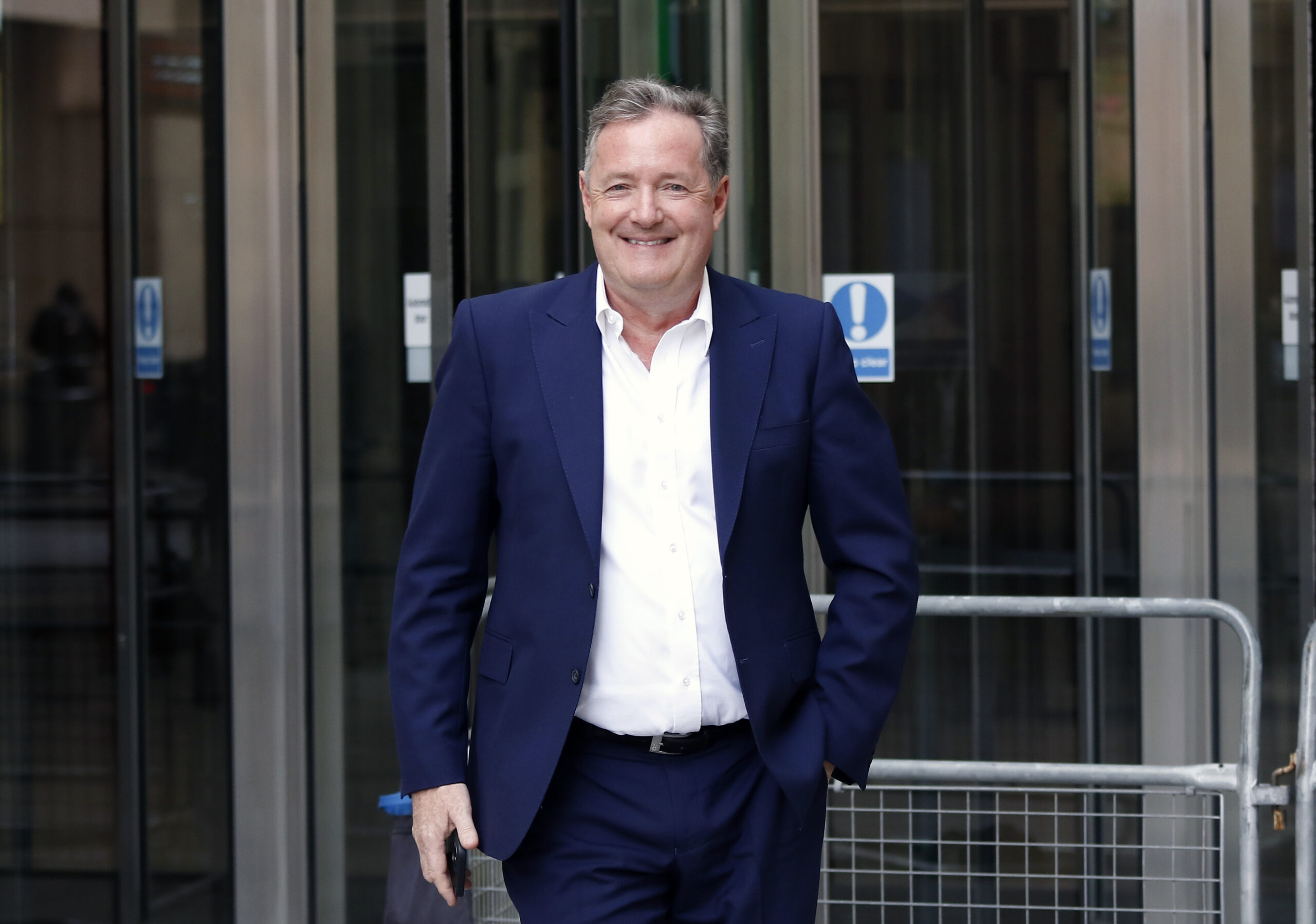 Piers Morgan smiling wearing a navy suit