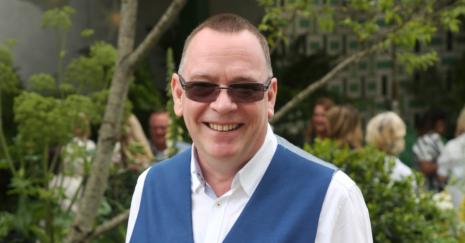 EastEnders star Adam Woodyatt smiling wearing sunglasses and a waistcoat (Credit: Splash)