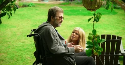 Derek Draper in a wheelchair, Kate Garraway squatting down next to him in the garden