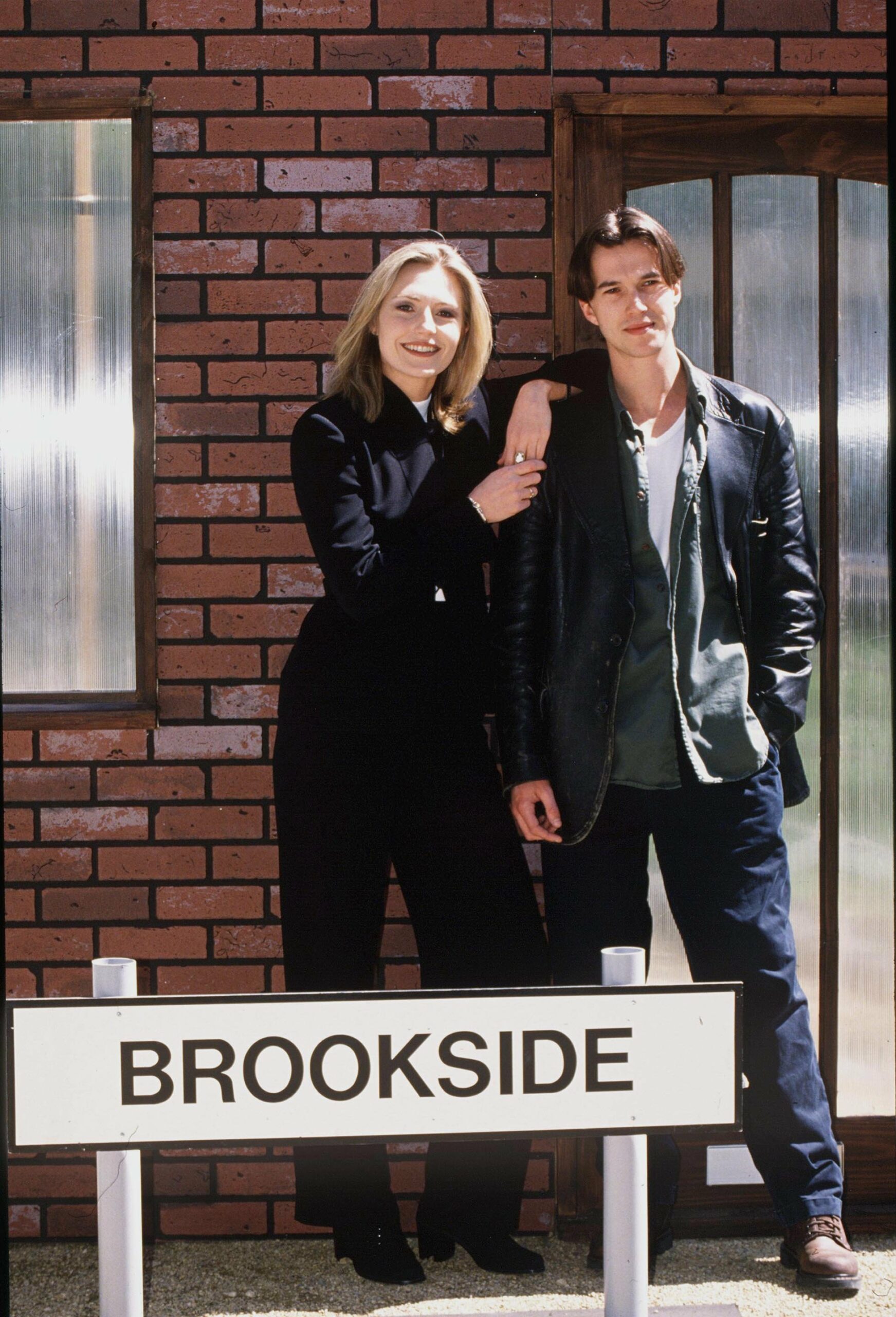 Brookside characters smiling outside a red brick house