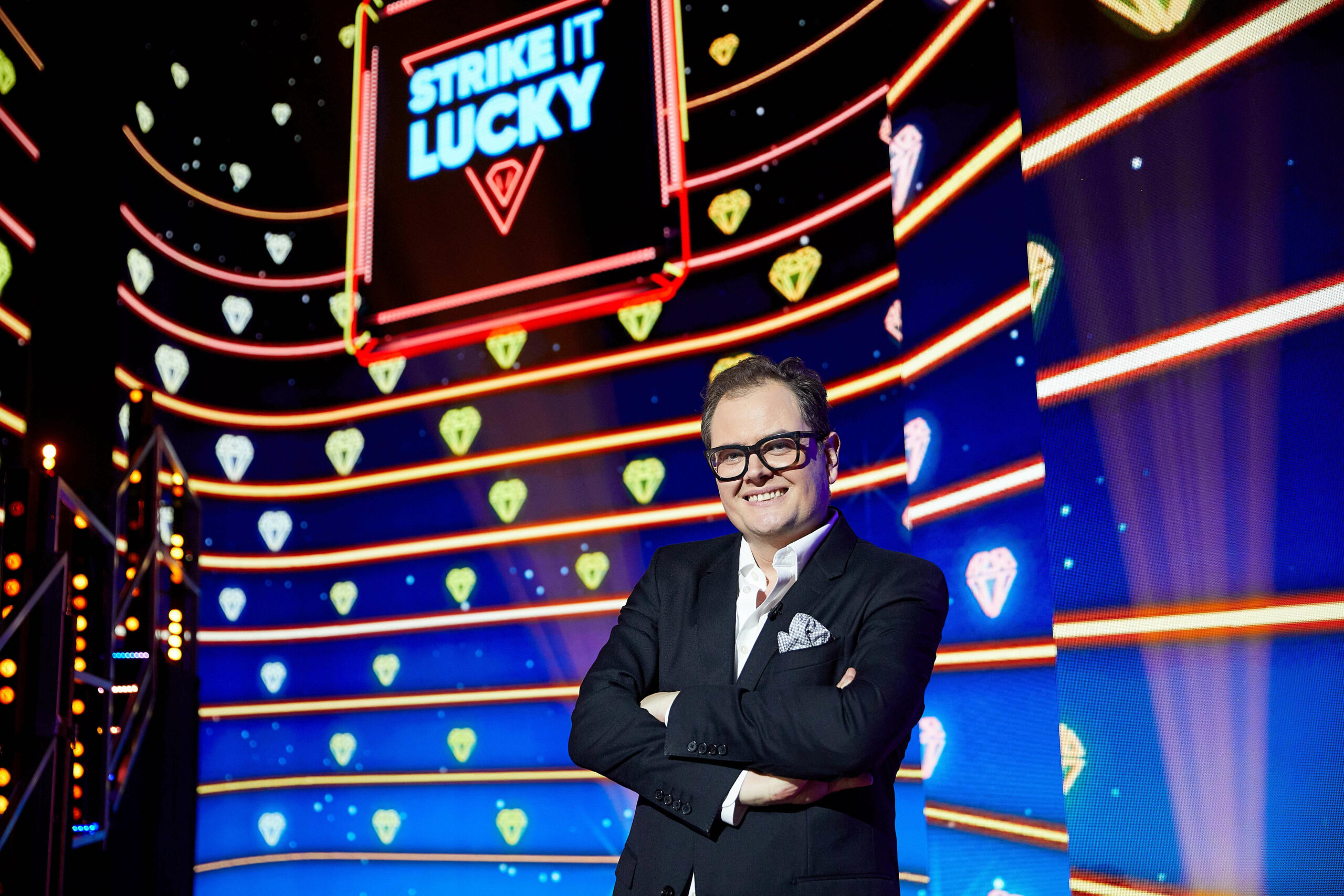 Alan Carr smiles in front of Strike It Lucky Sign