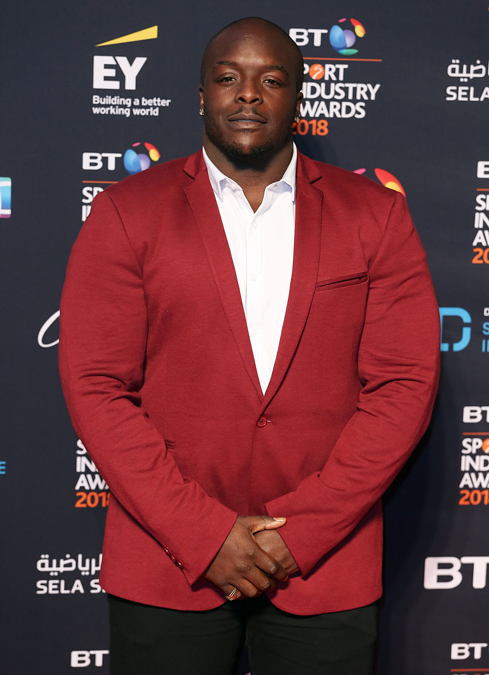 Adebayo Akinfenwa smiling in red suit at event