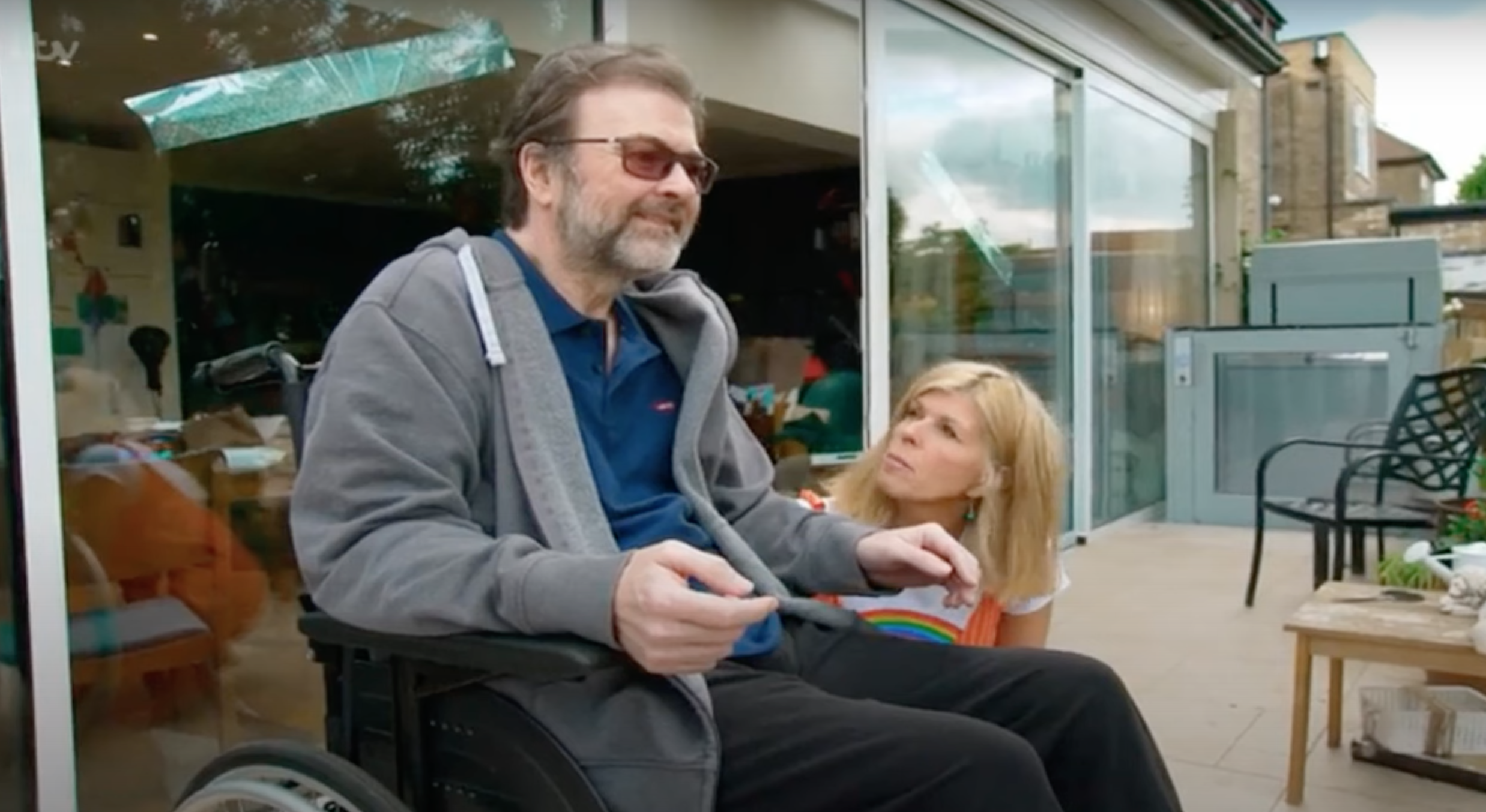 Derek Draper in a wheelchair, Kate Garraway squatting next to him