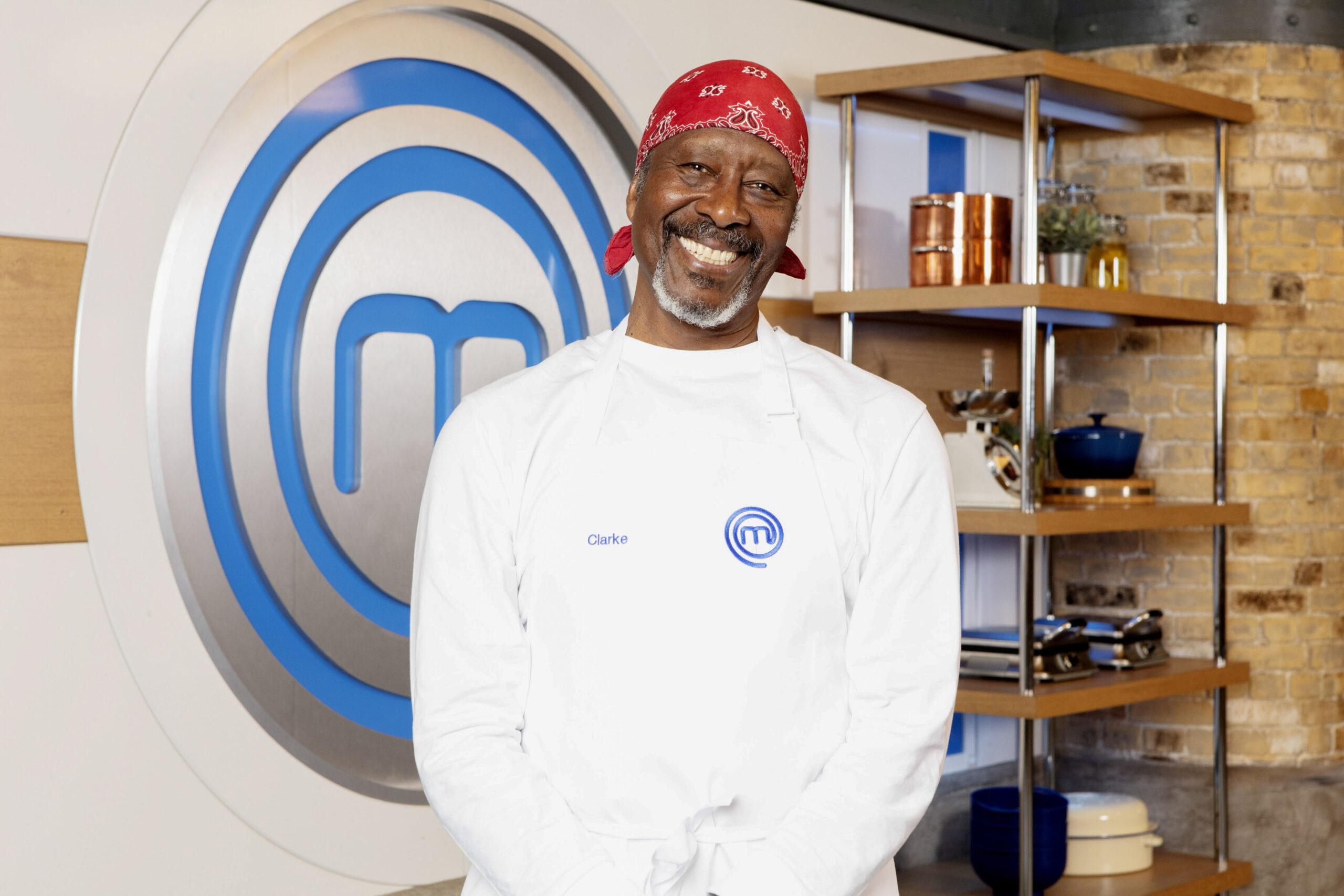 Clarke Peters poses in chef whites next to the Masterchef logo