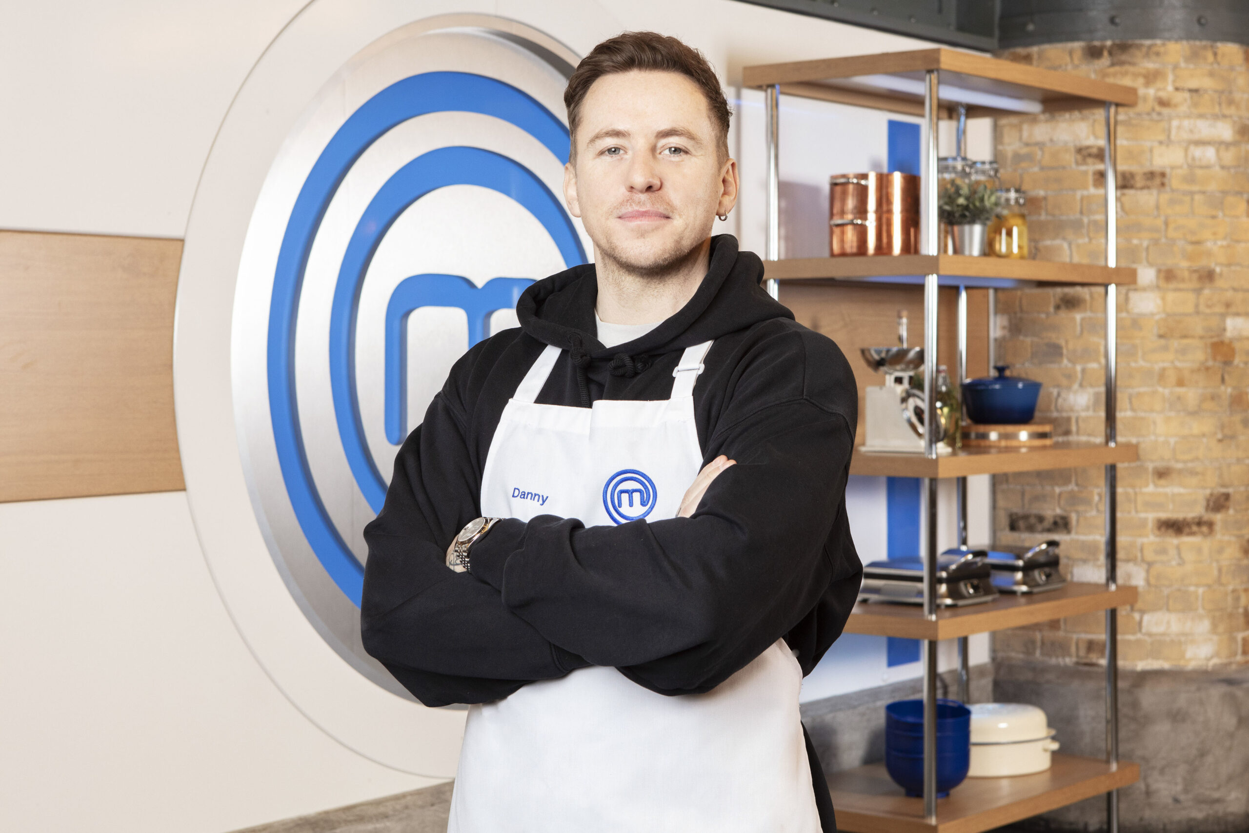 Danny Jones poses with arms folded with his Masterchef apron on