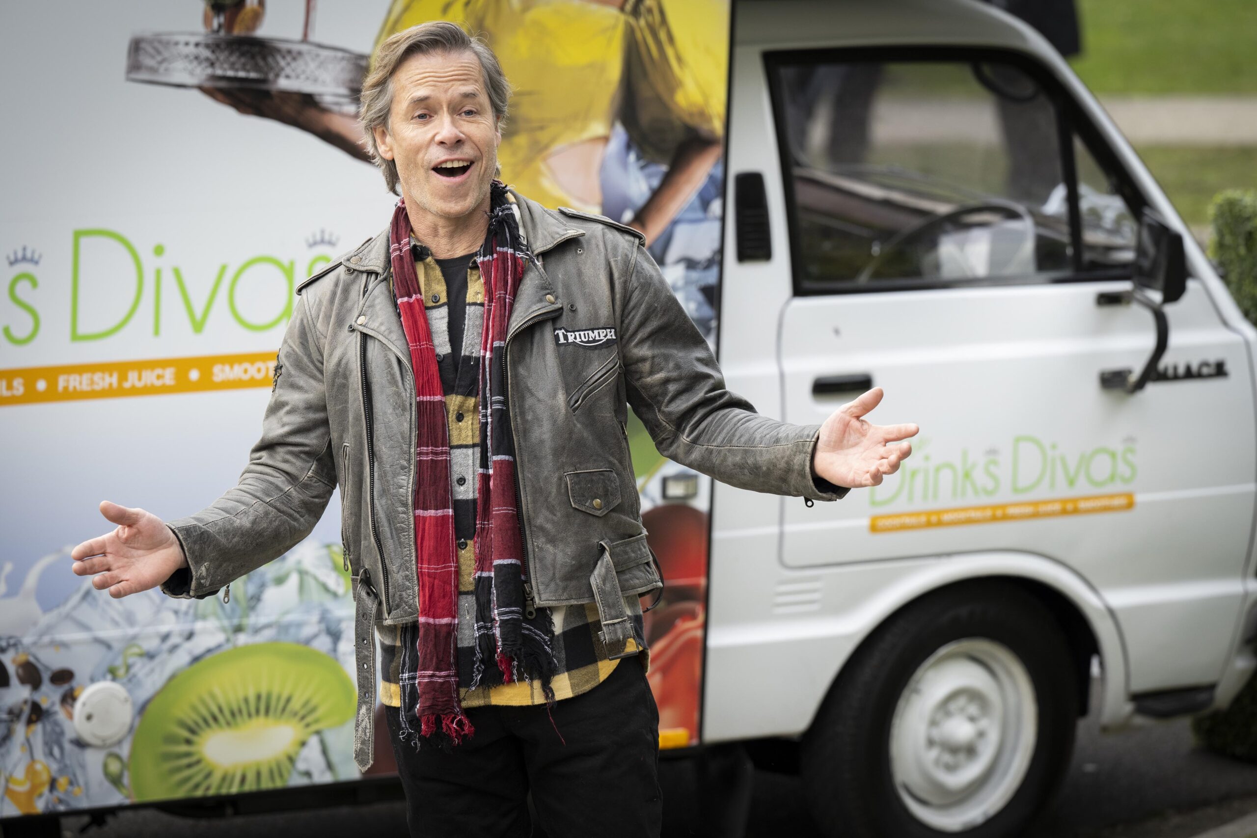 Guy Pearce stands with open arms infront of a 'Drinks Divas' truck on the set of Neighbours. 