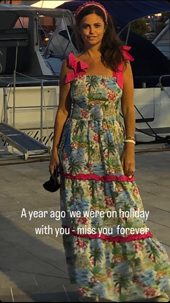 Dame Deborah James stands in a sundress while on holiday. There is text which reads 'A year ago we were on holiday with you - miss you forever'