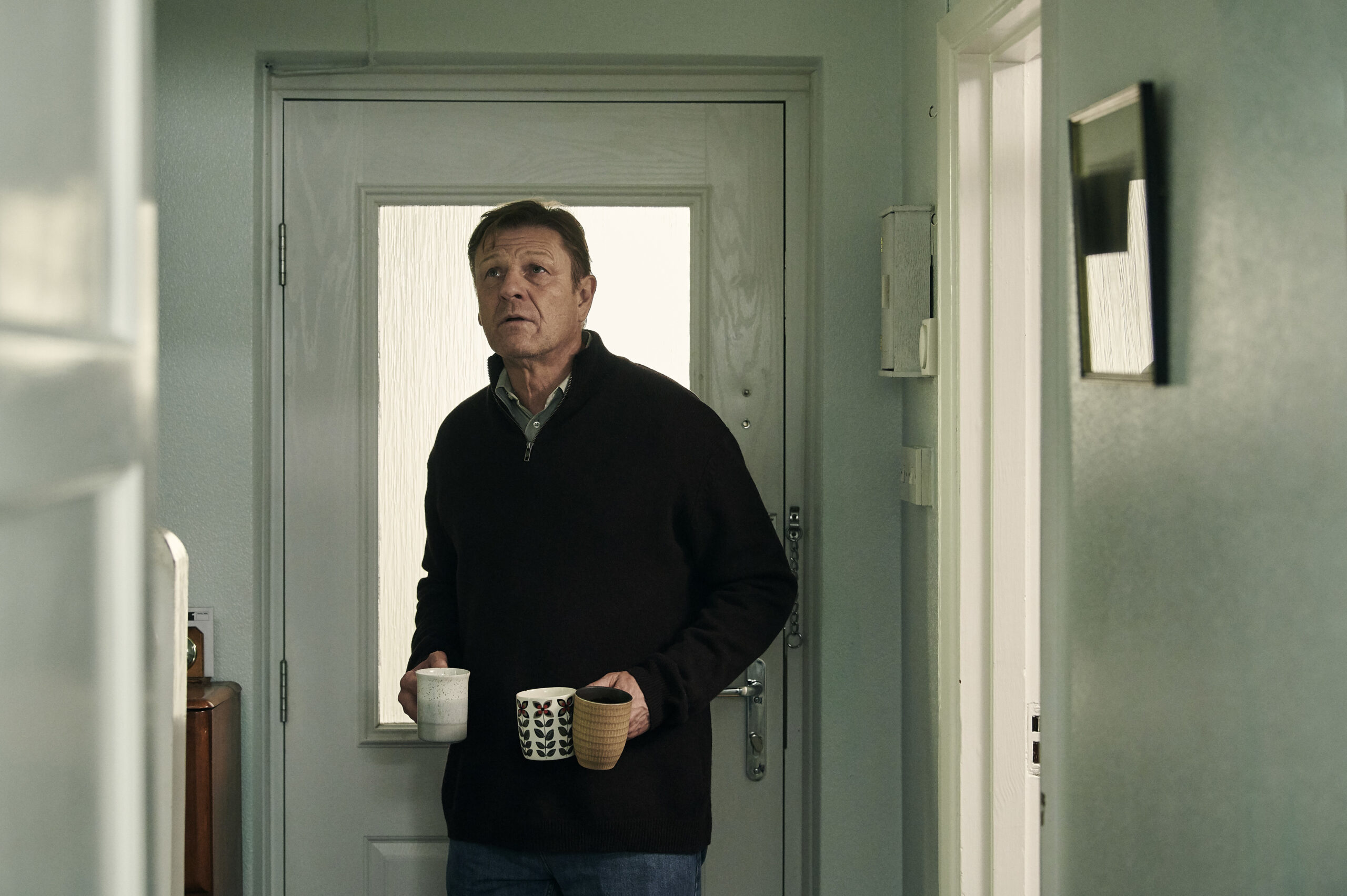 Sean Bean as Ian, he holds two mugs at the front door in Marriage on BBC