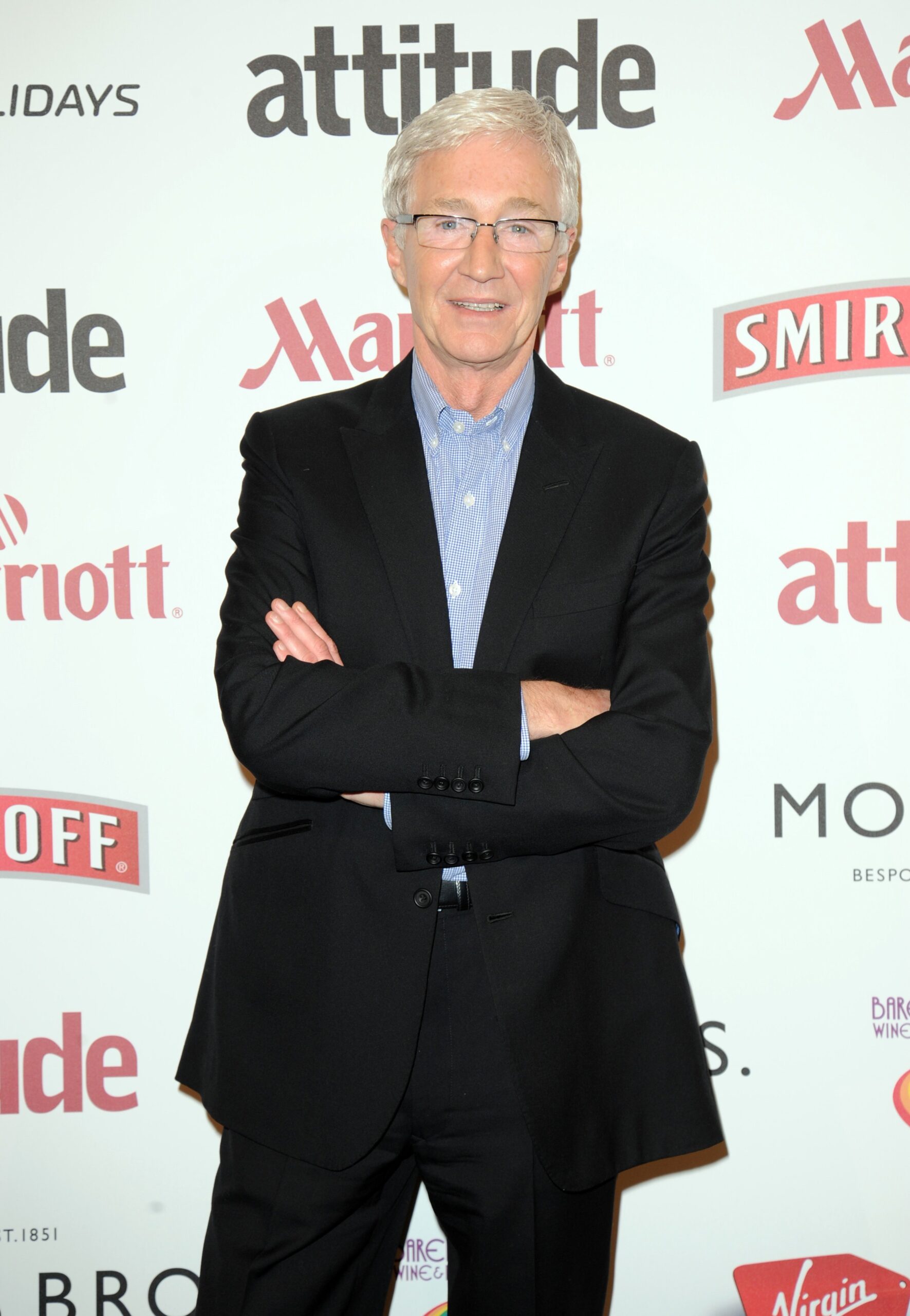 Paul O'Grady smiles with arms crossed on red carpet. 
