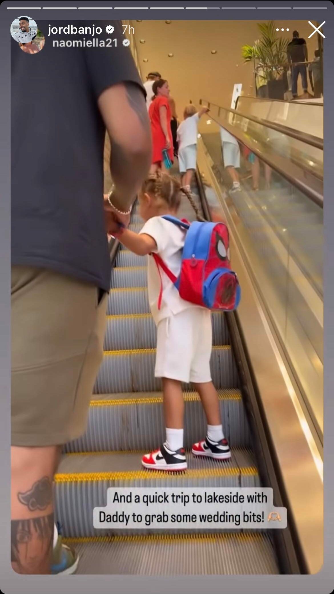Jordan Banjo holds his child's hand while going up an escalator