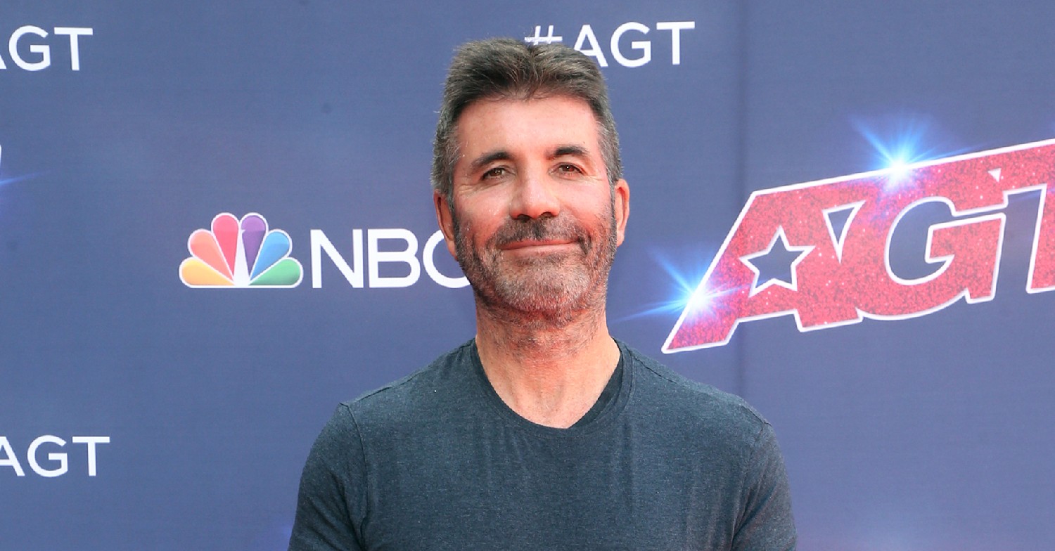 Simon Cowell in a grey top, smiling at a red carpet event